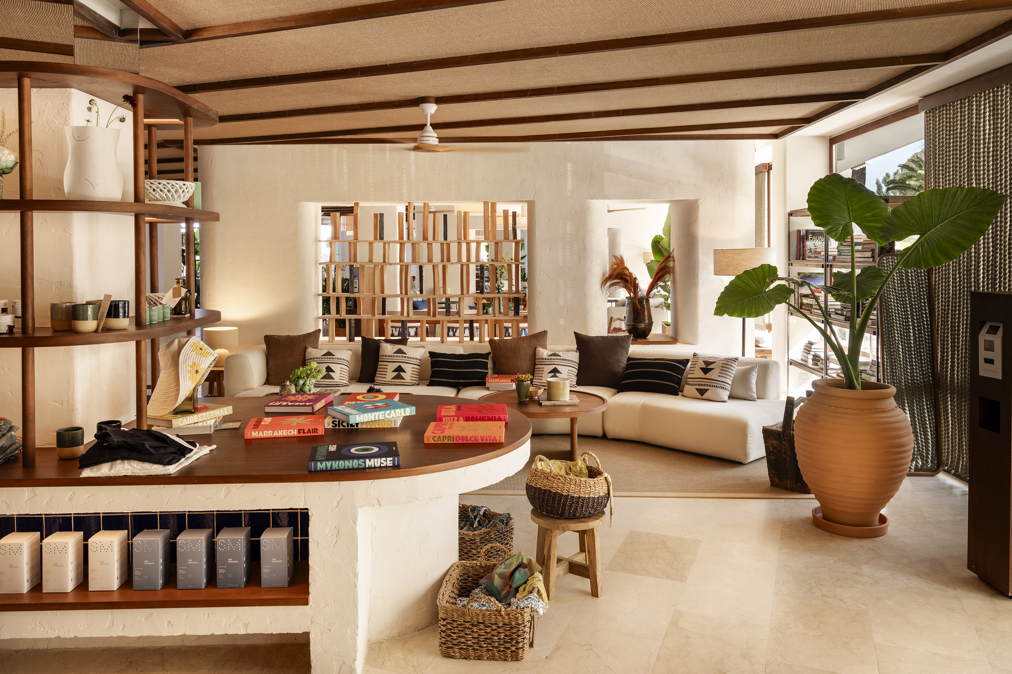 Elegant resort lounge with white sofa, coffee table books, lush plant, wood ceiling.