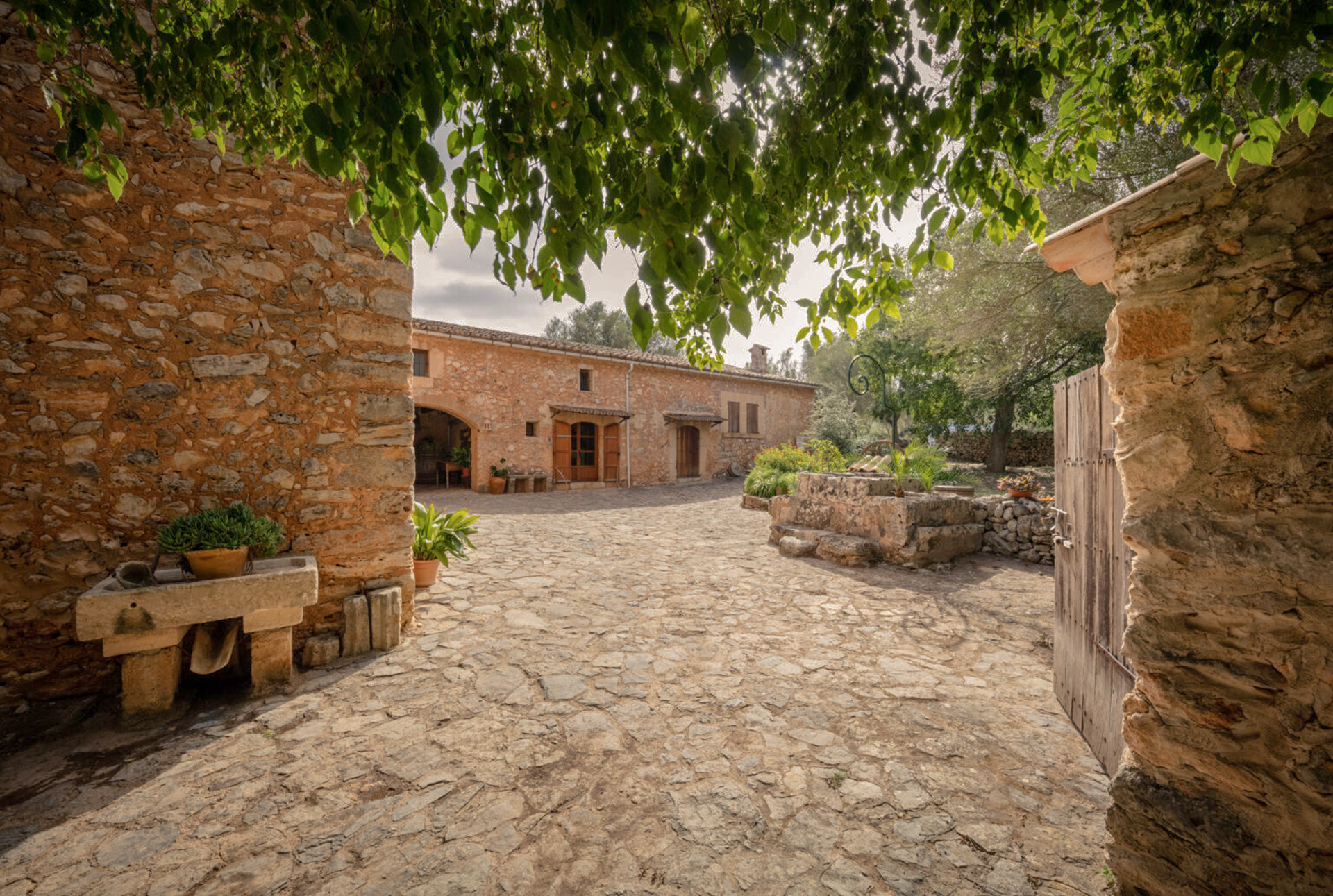 Finca mallorquina de piedra con patio empedrado bajo follaje verde.