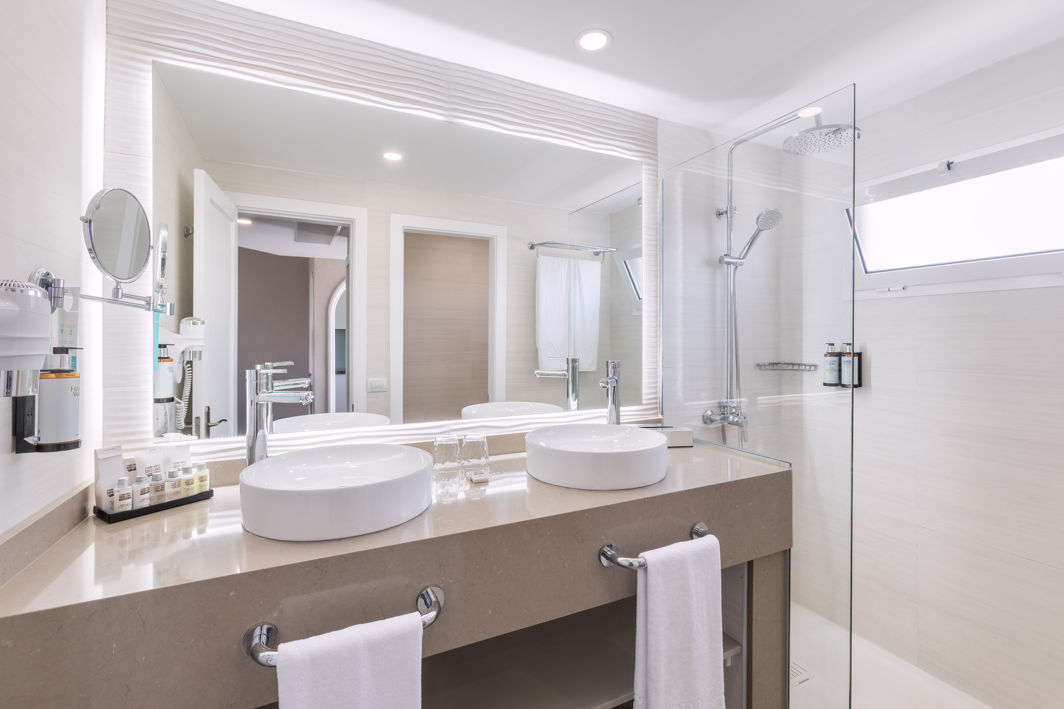 Bright modern hotel bathroom with double vanity, large mirror, and glass shower.