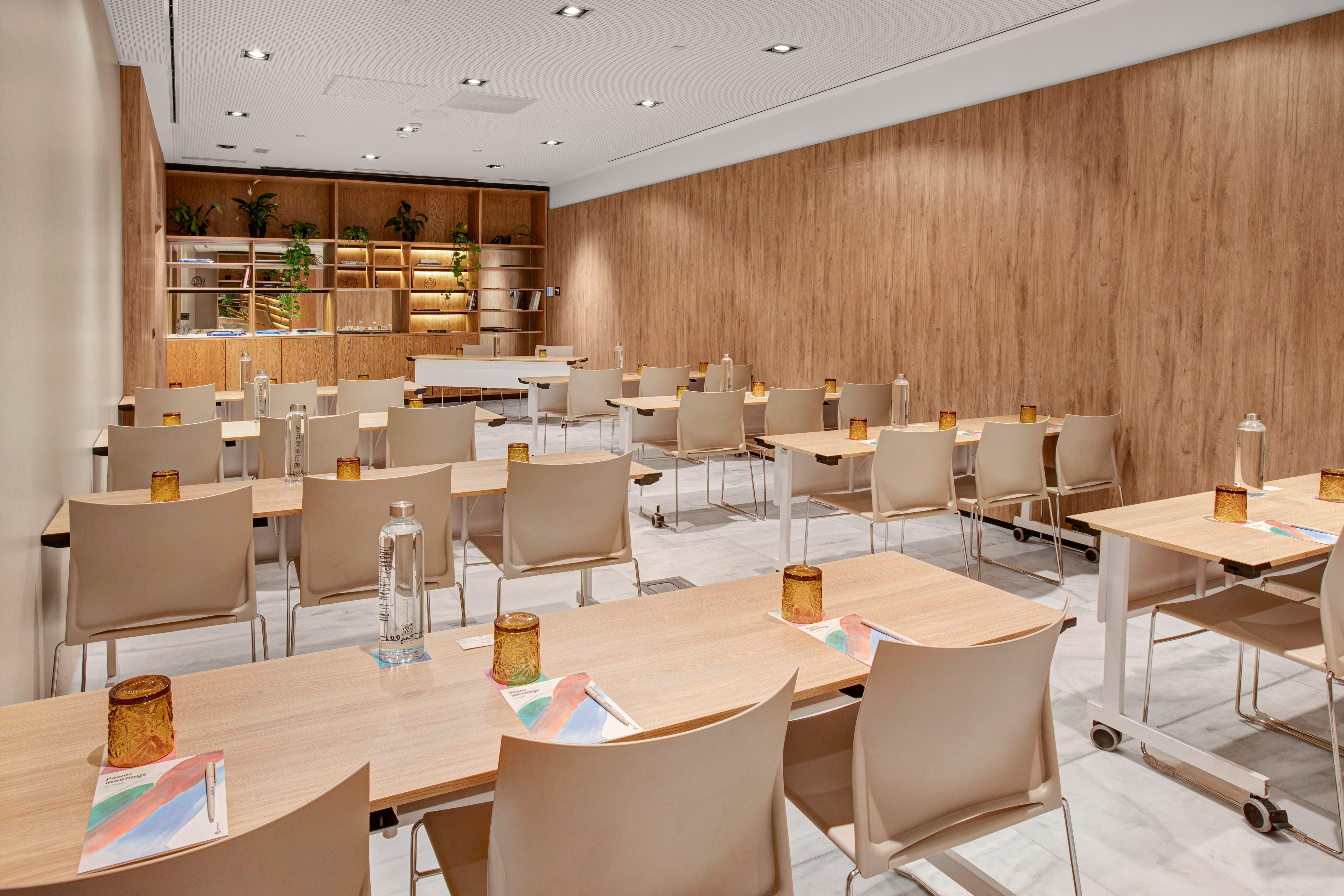Contemporary meeting room setup with wood tables, beige chairs, and green plants.