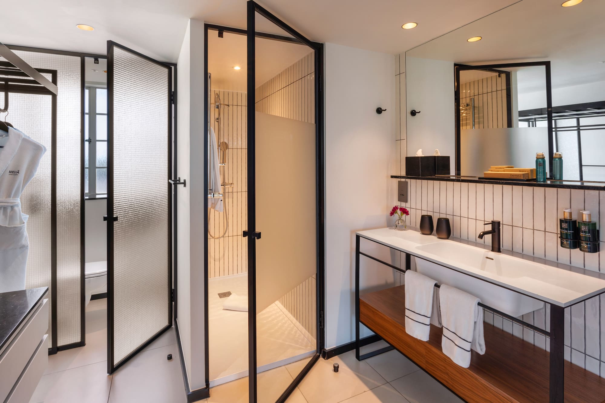 Modern hotel bathroom with black-framed glass shower and white vanity.