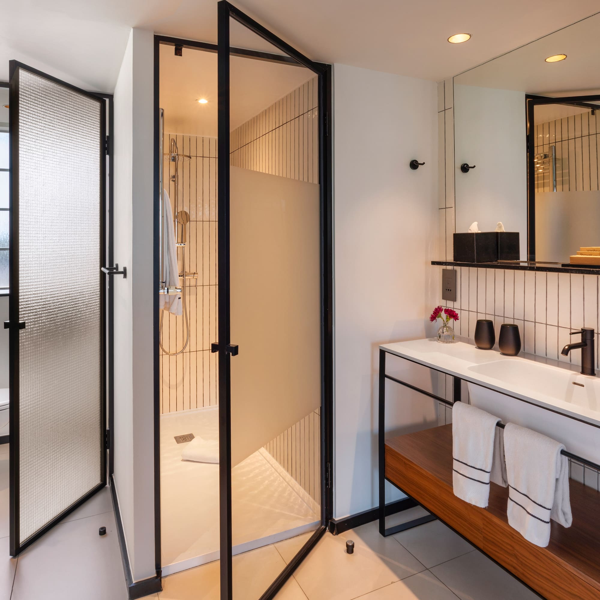 Sleek hotel bathroom with glass shower, floating vanity, and black accents.