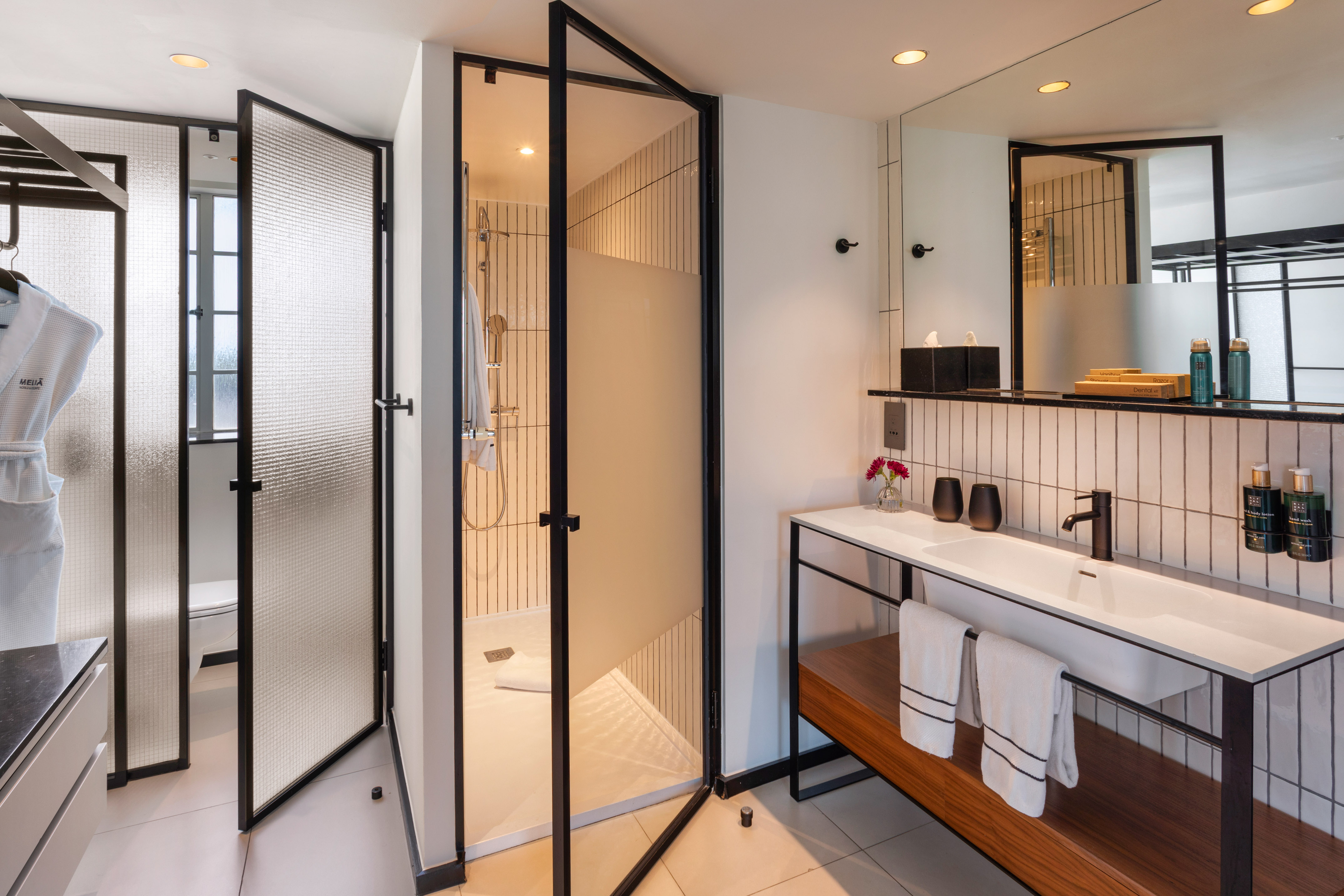 Modern hotel bathroom with black-framed glass shower and white vanity.
