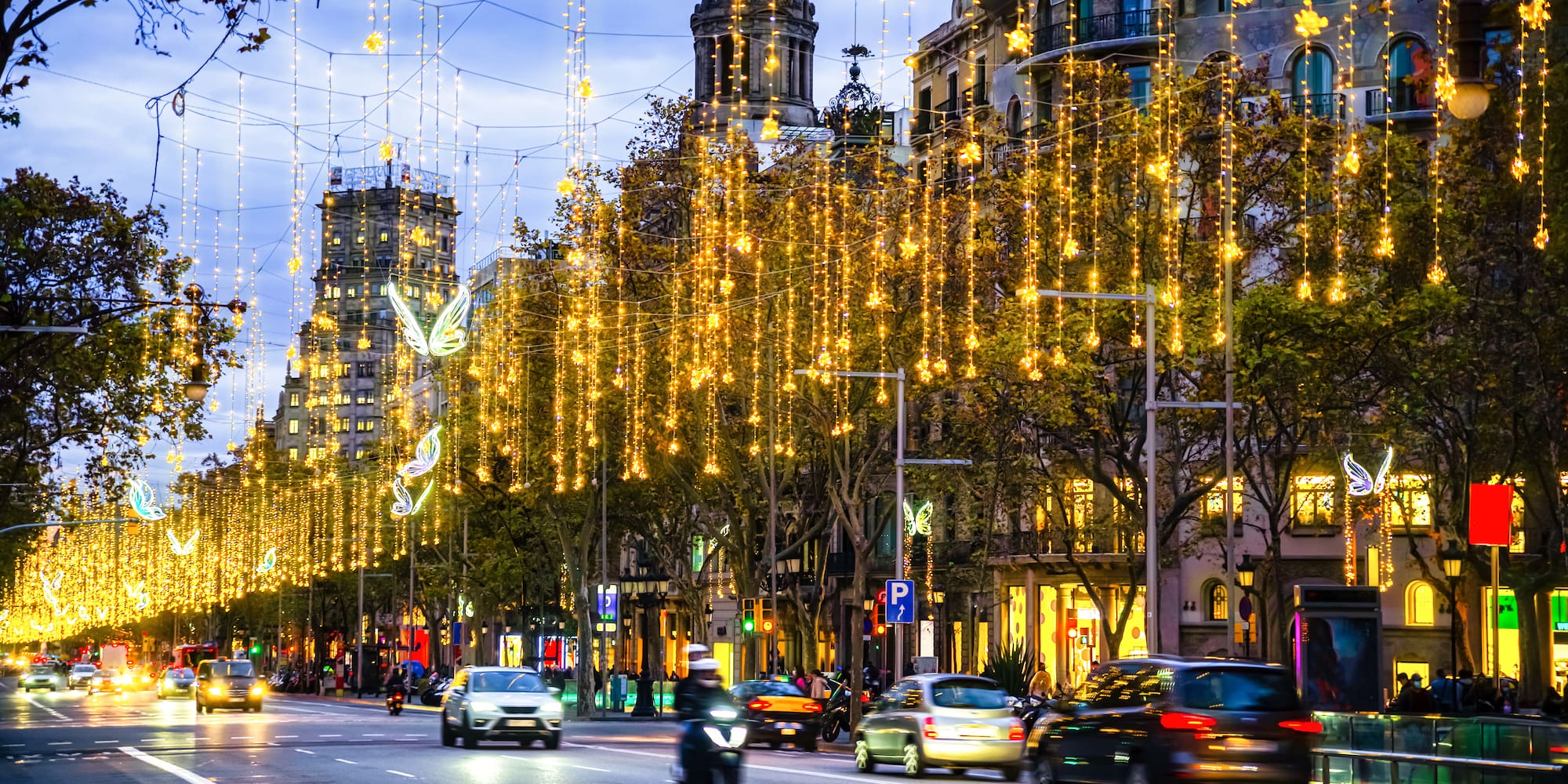 Luces de Navidad doradas iluminando avenida urbana con tráfico nocturno.
