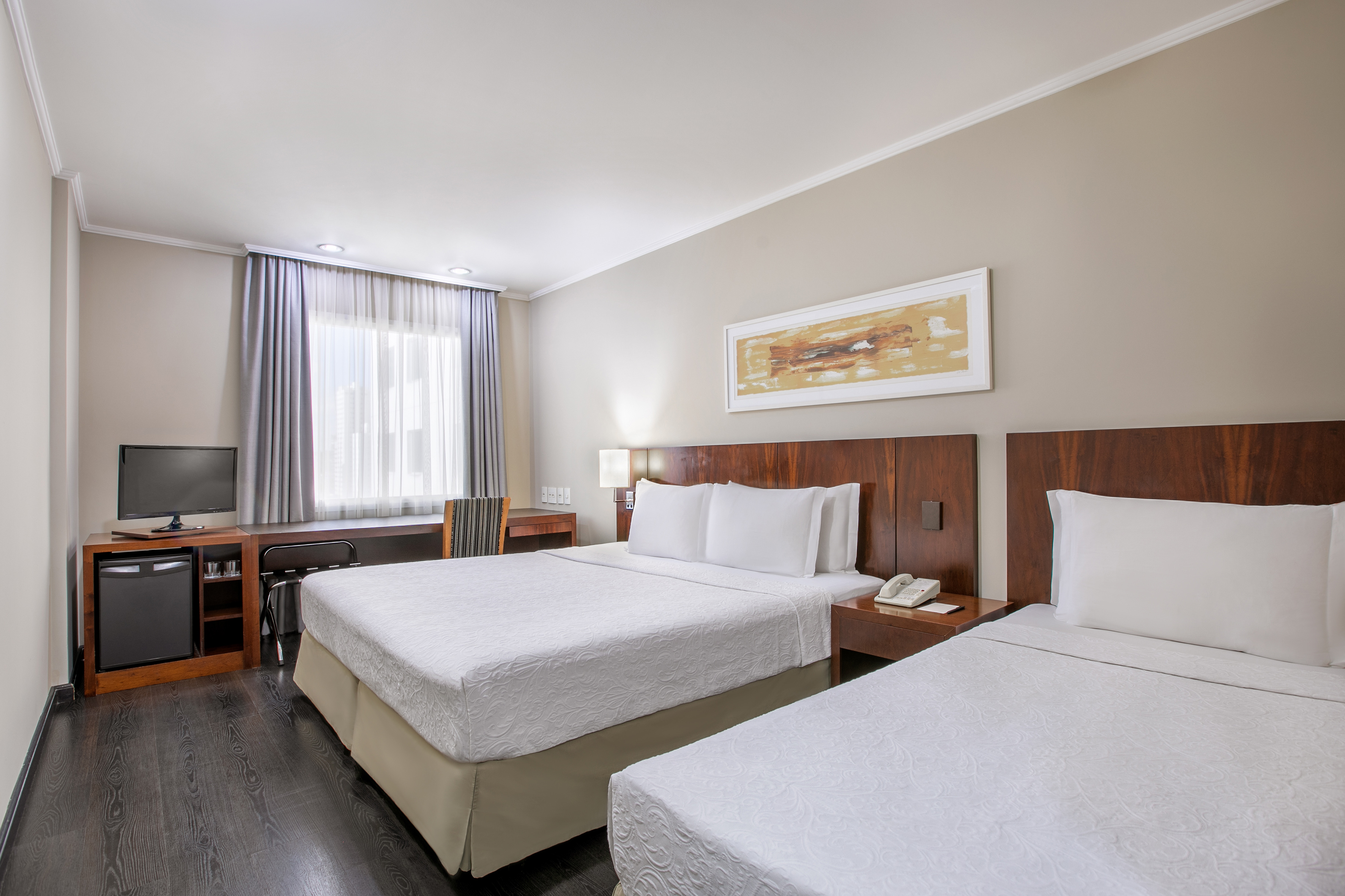 Hotel room with two double beds, desk, TV, and dark wood floor.