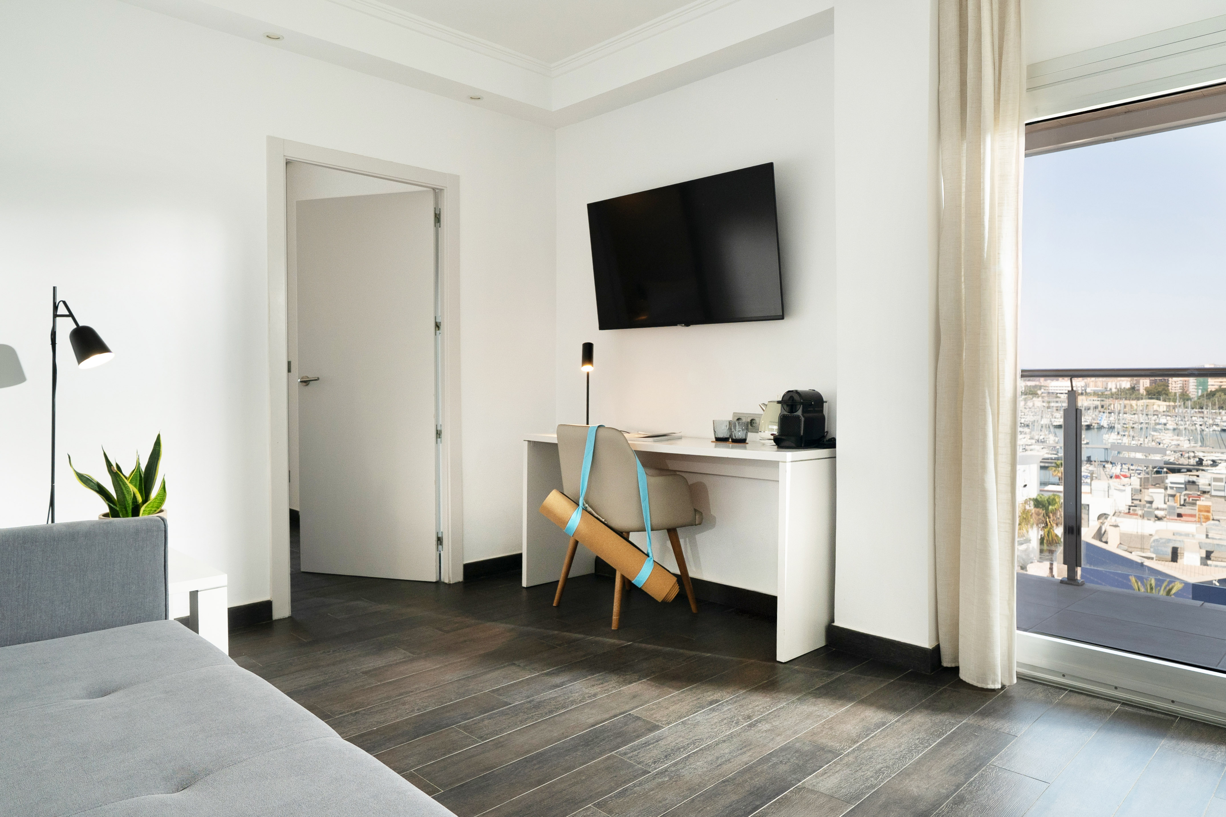 Modern hotel room workspace with marina view, TV, coffee, and yoga mat.