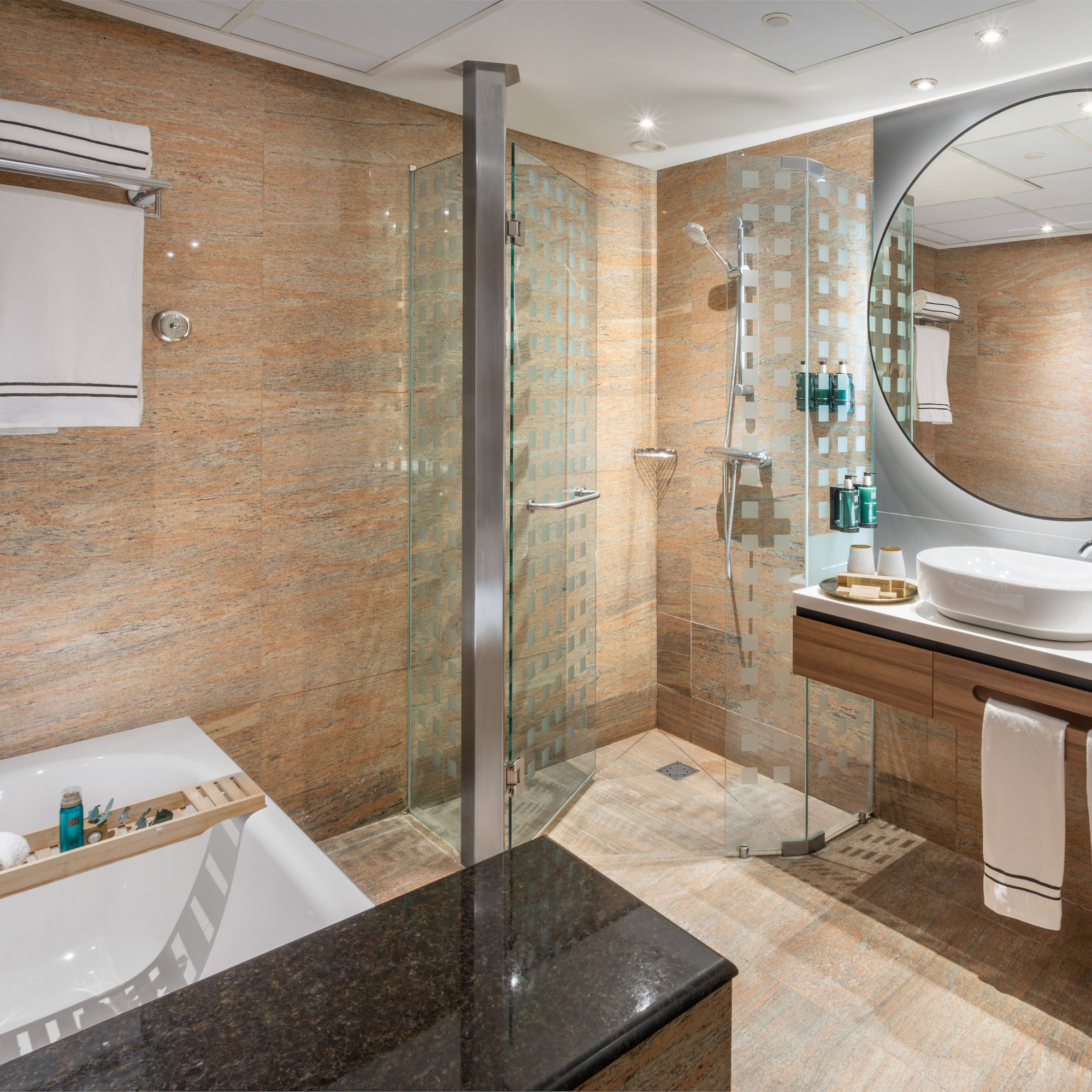 Baño moderno con ducha de cristal, bañera, lavabo flotante y espejo redondo.