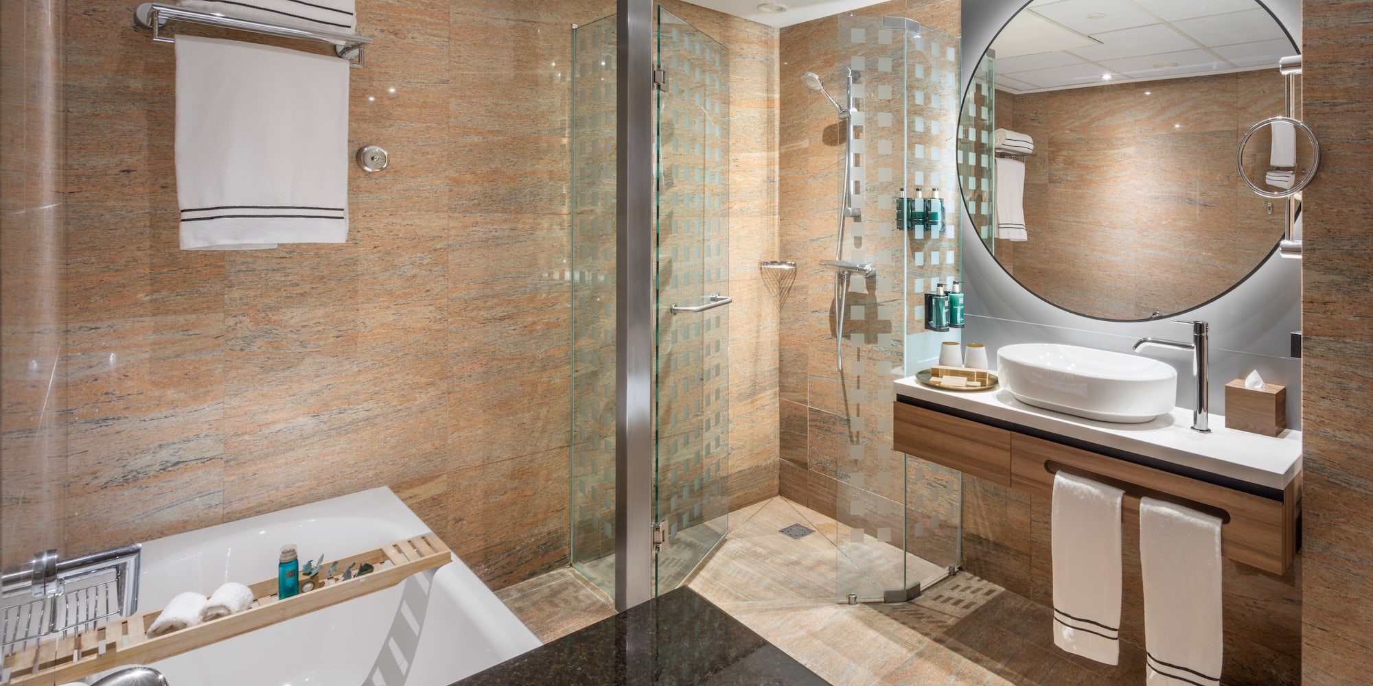 Baño moderno con ducha de cristal, bañera, lavabo flotante y espejo redondo.