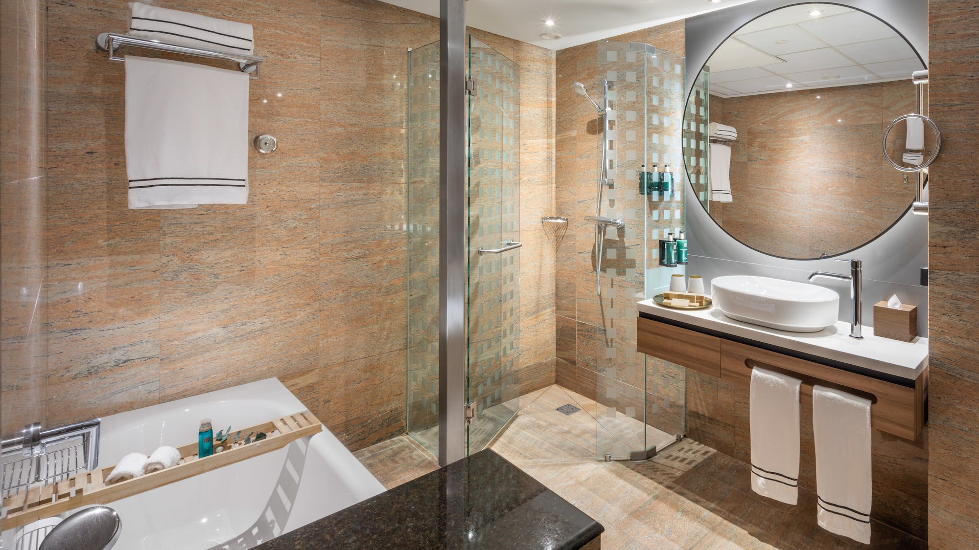 Baño moderno con ducha de cristal, bañera, lavabo flotante y espejo redondo.