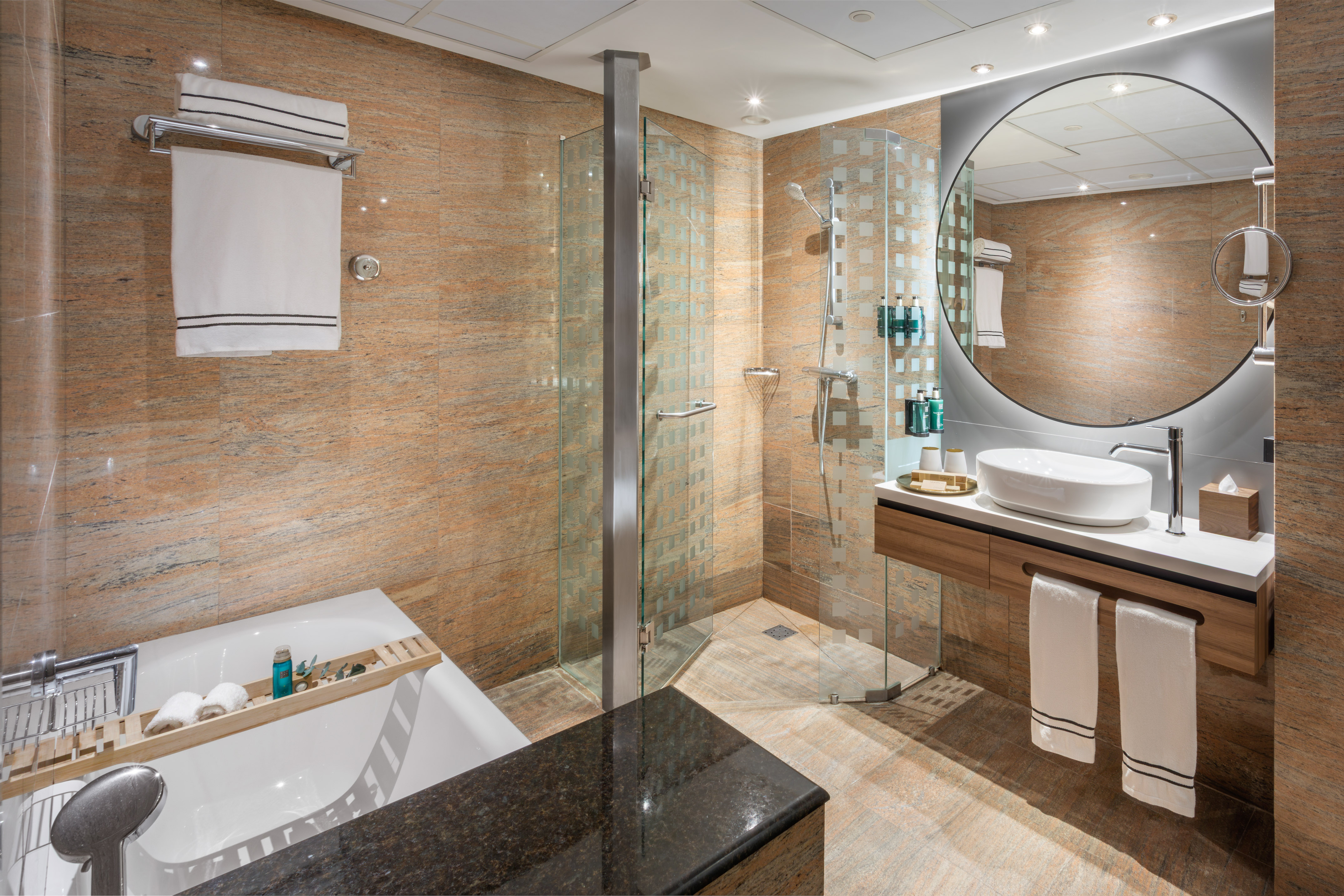 Baño moderno con ducha de cristal, bañera, lavabo flotante y espejo redondo.