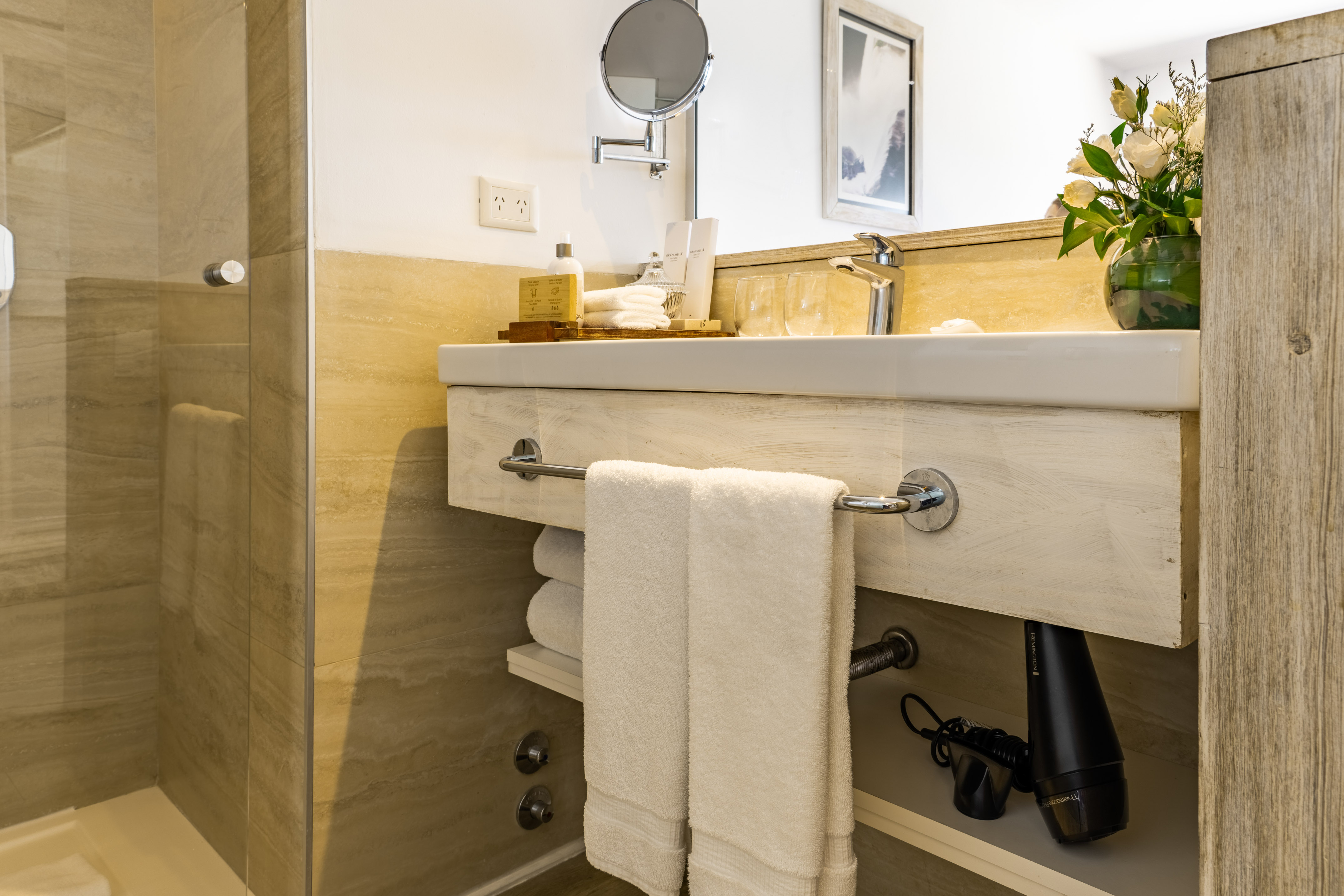 Hotel bathroom with white sink, light wood vanity, fresh towels & glass shower.