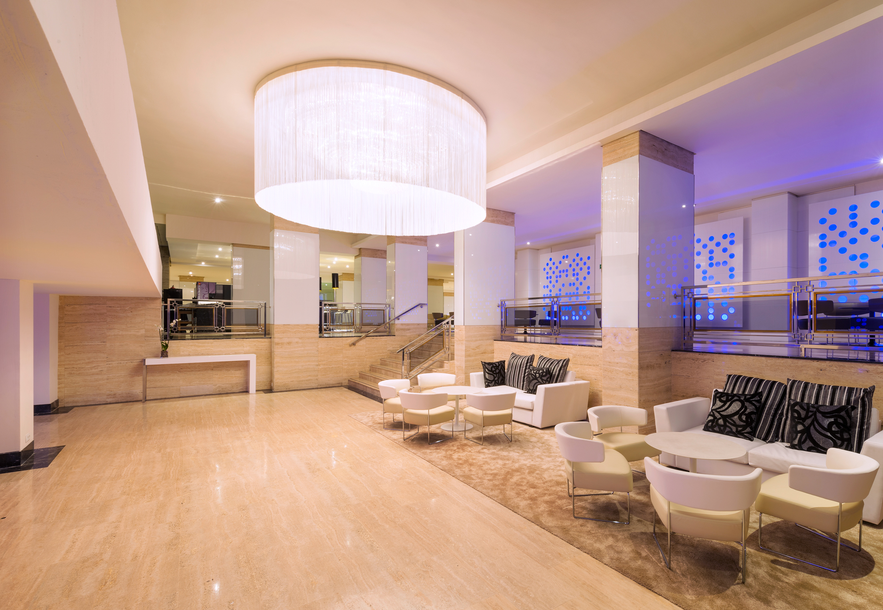 Elegant hotel lobby lounge with white seating, chandelier, and blue wall lighting.