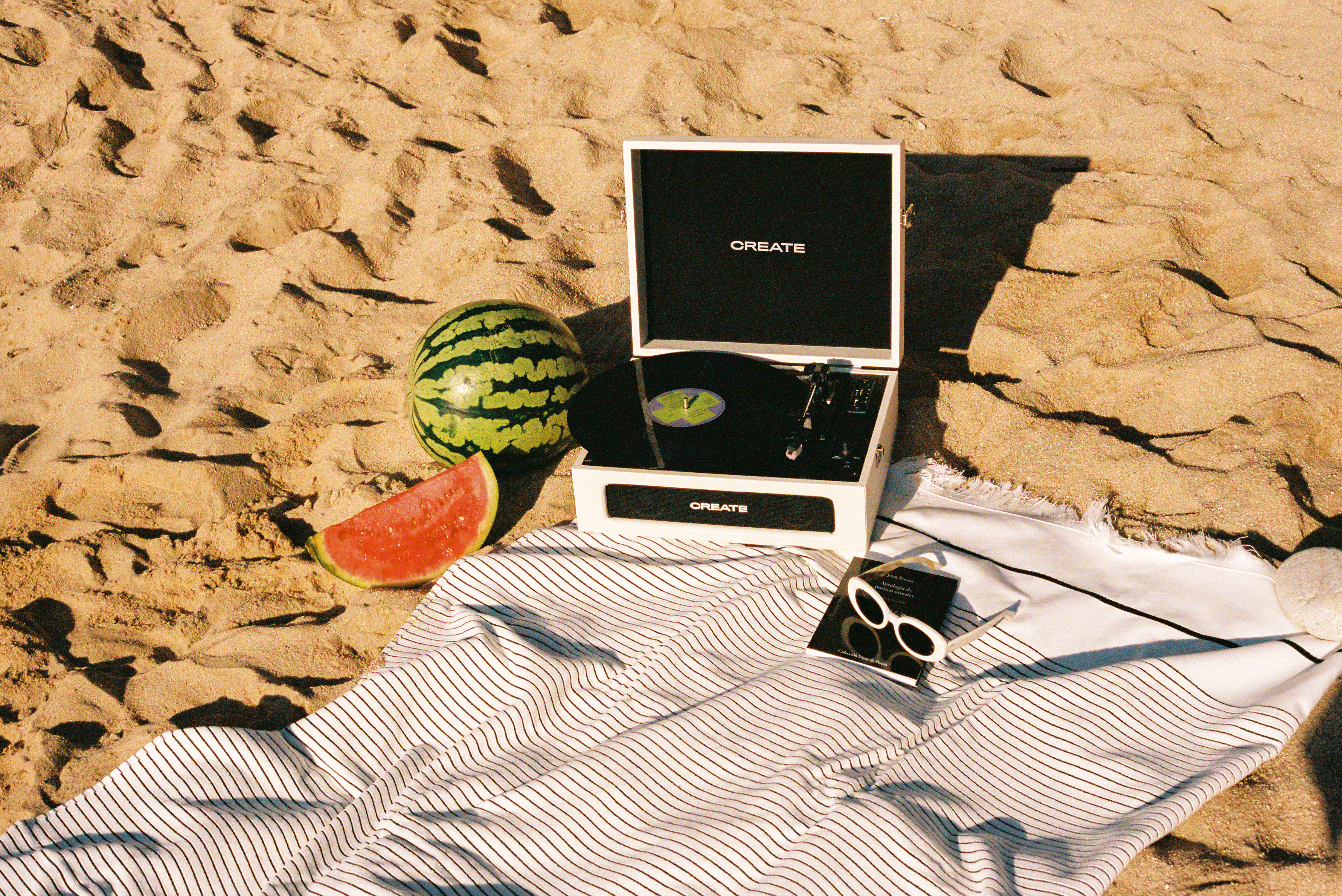 Portable record player, watermelon, and sunglasses on striped beach towel.