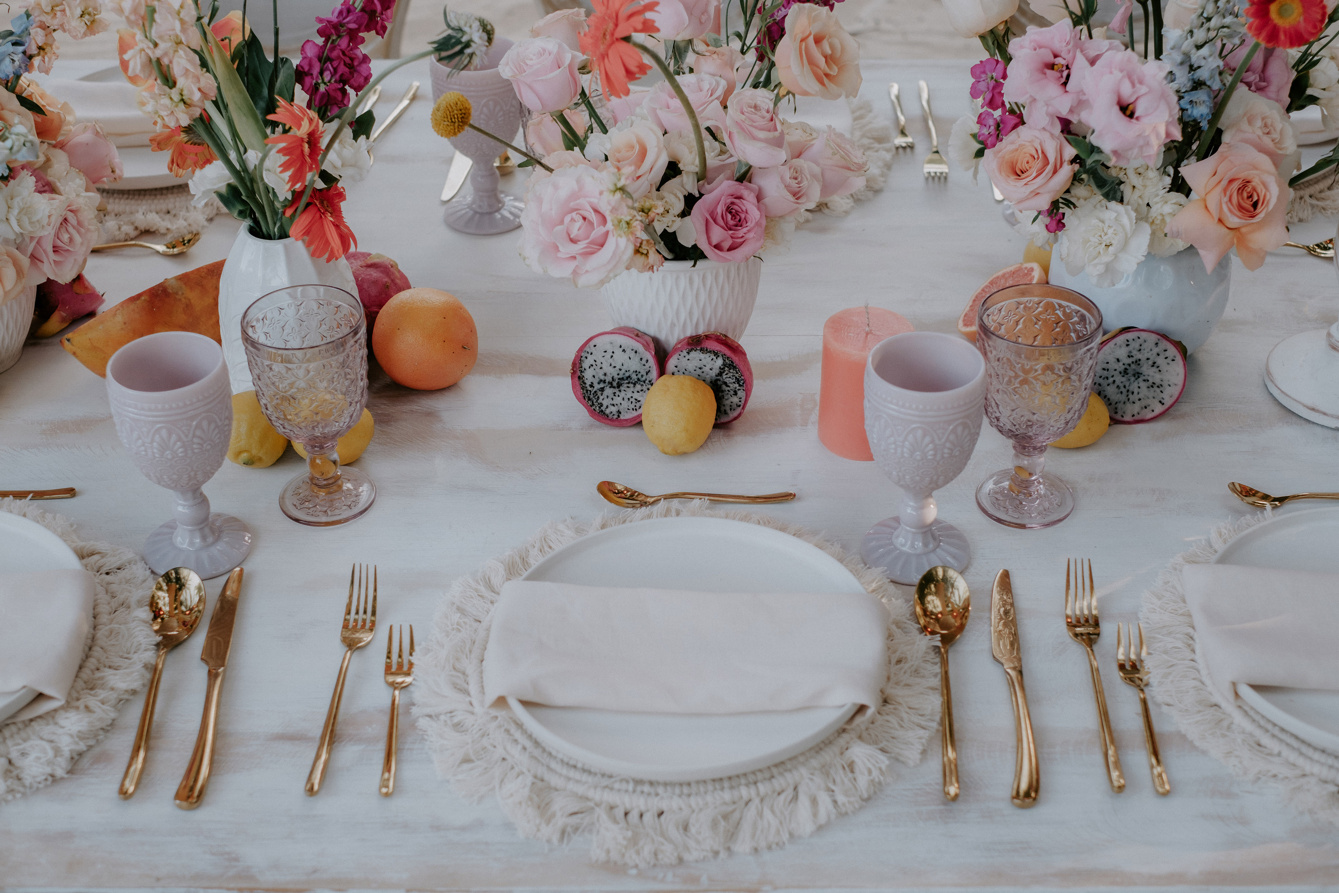 Boho chic table with pastel flowers, gold flatware, and tropical fruit.