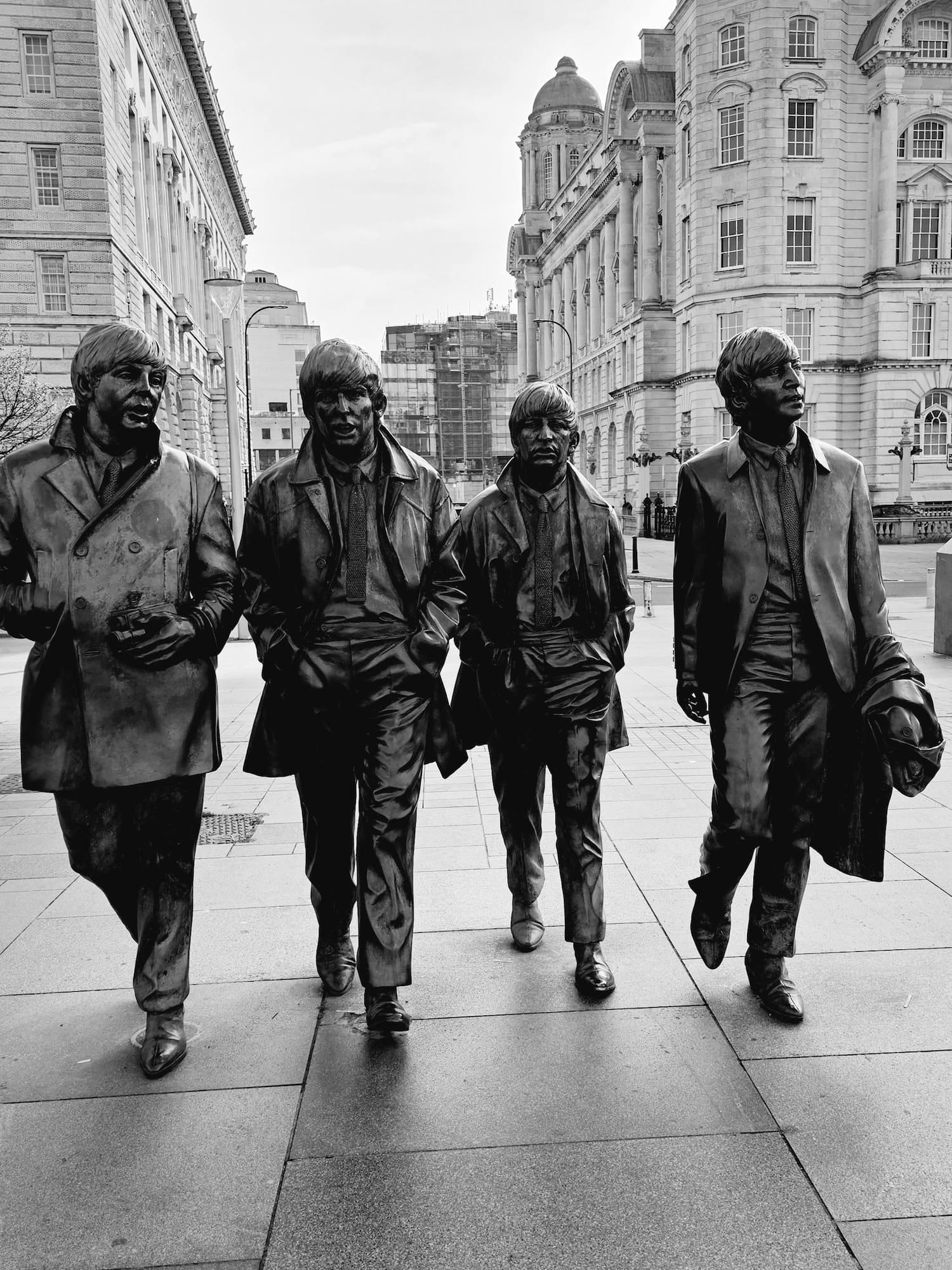 Black and white bronze statues of The Beatles walking in Liverpool.