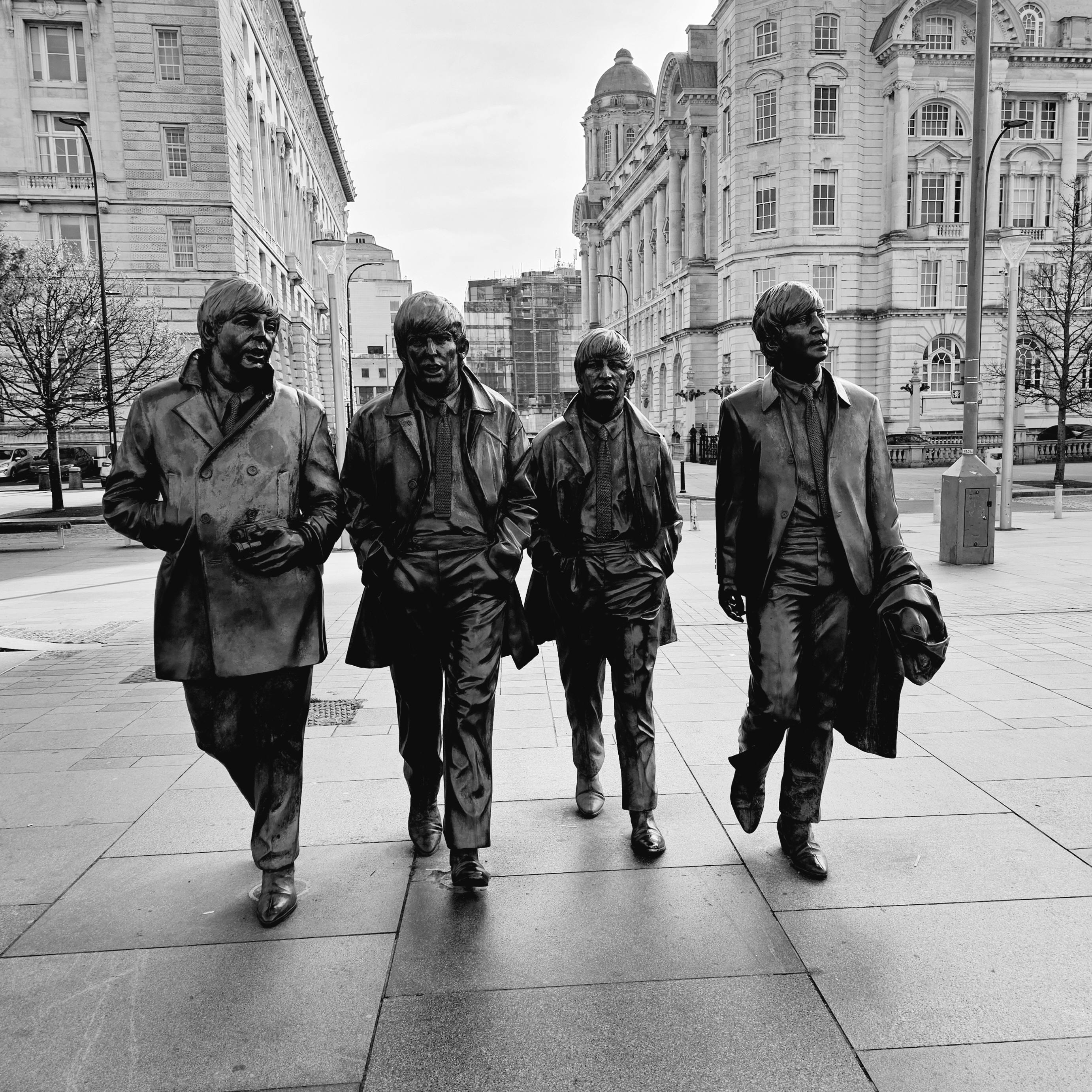 Black and white bronze statues of The Beatles walking in Liverpool.