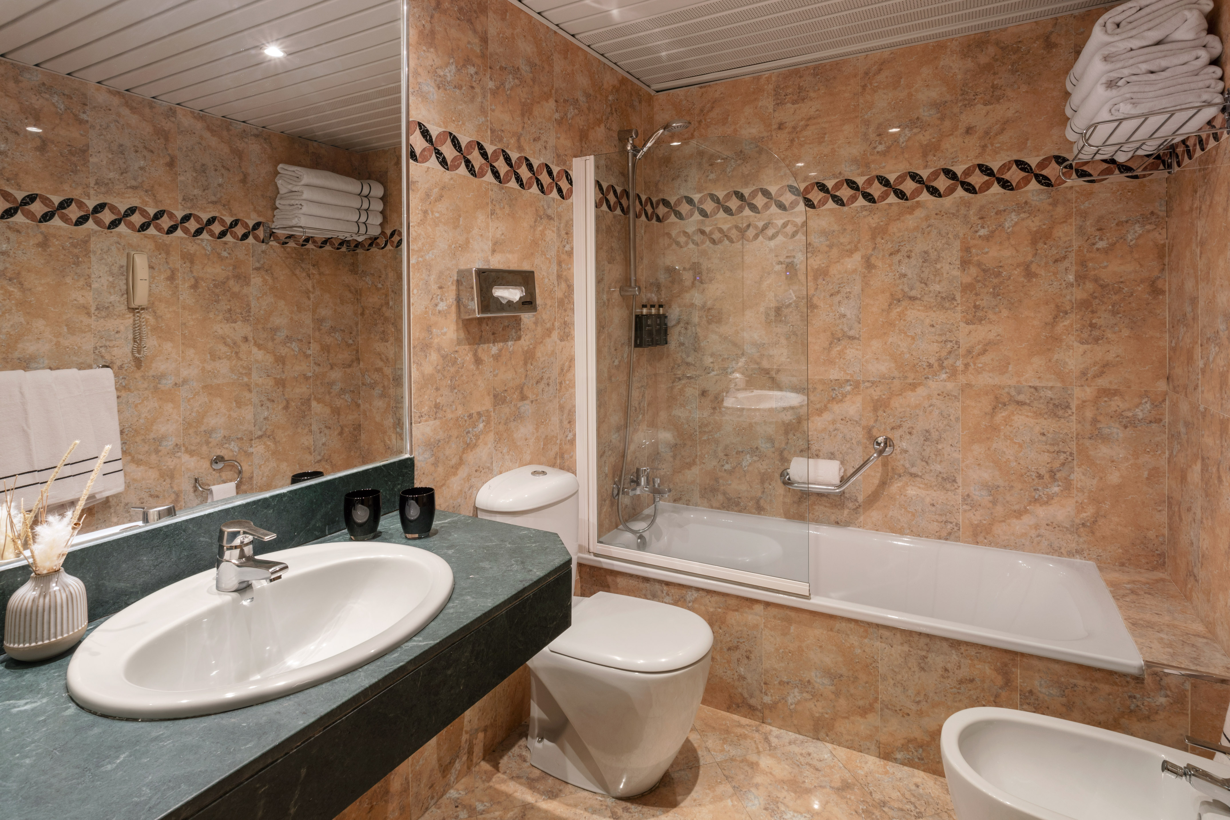 Tiled hotel bathroom with vanity, sink, toilet, bidet, and tub with shower.