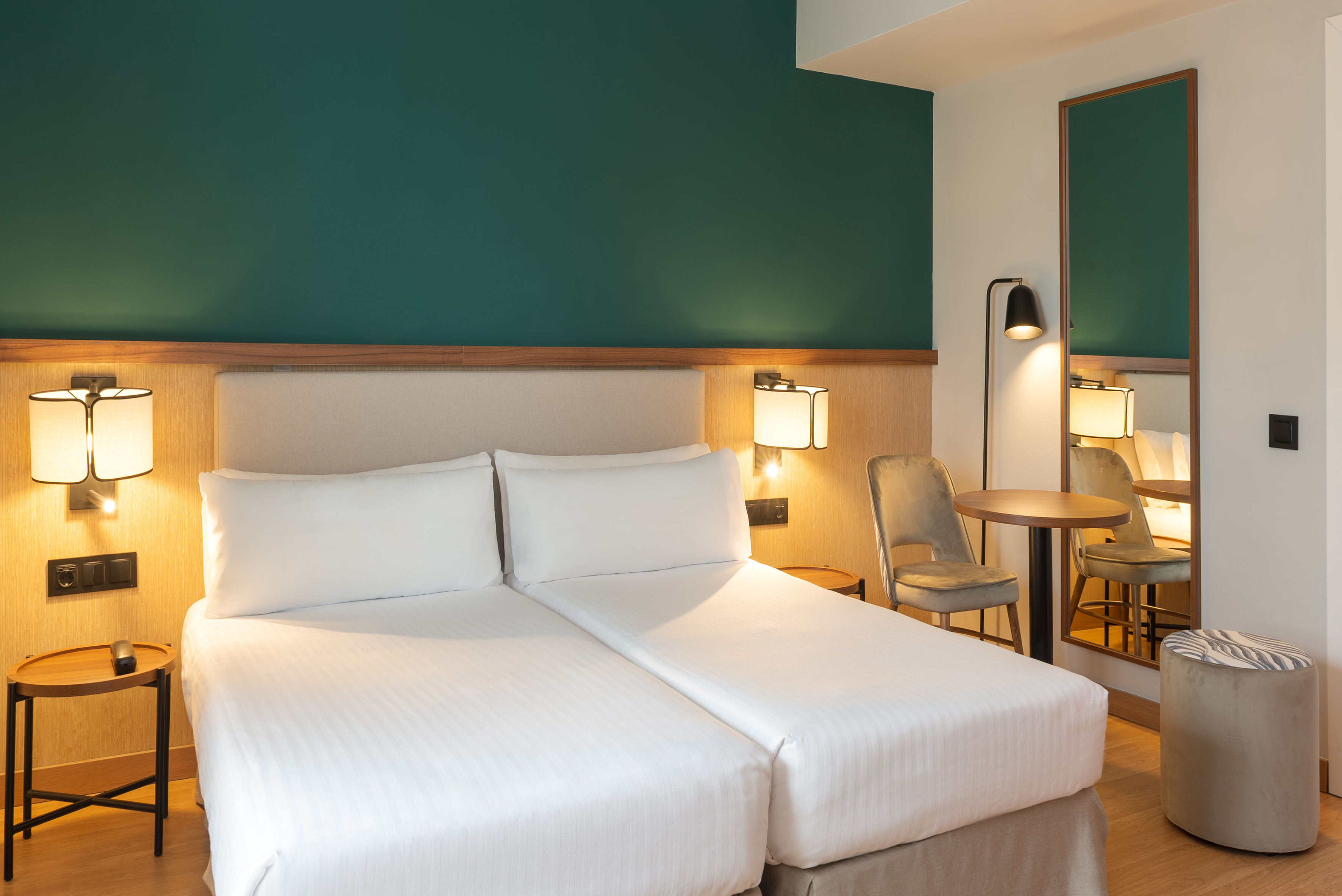 Comfortable hotel room with twin beds, teal wall, and stylish modern furniture.