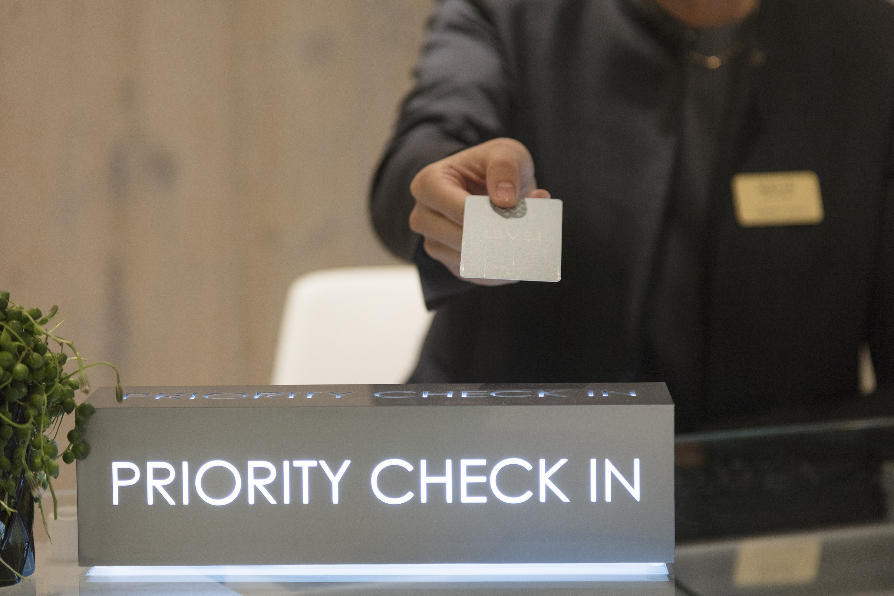 Hotel staff offering a room key at a lit "Priority Check In" counter. - The Level at Meliá White House, Londres