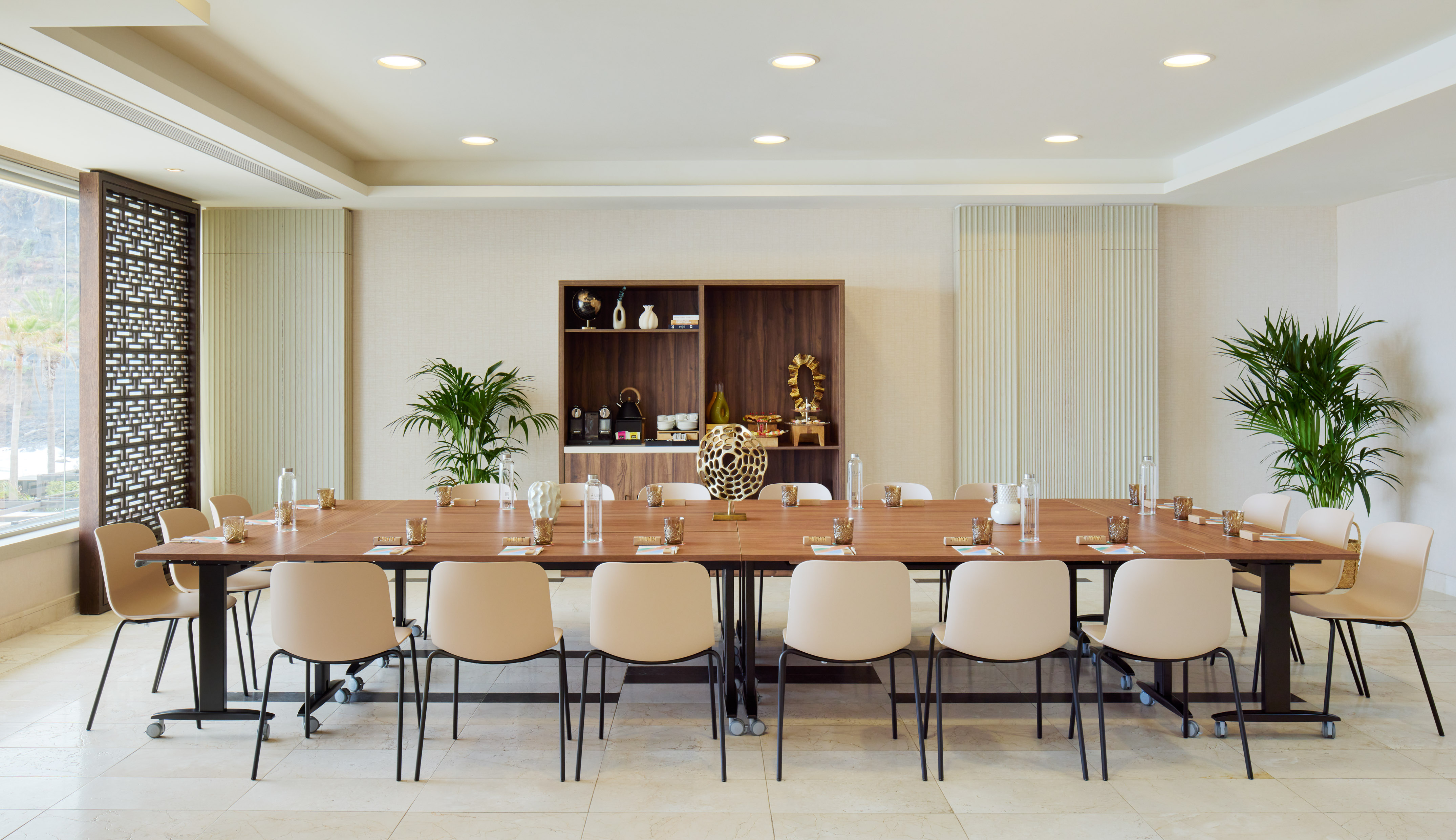 Business meeting room with wooden table, beige chairs, and refreshment station.