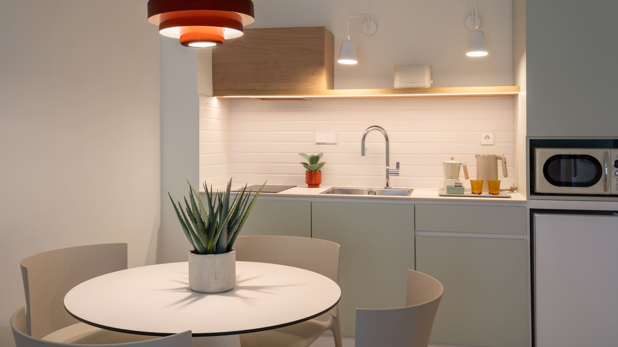 Modern kitchenette and dining area with red pendant light and round table.
