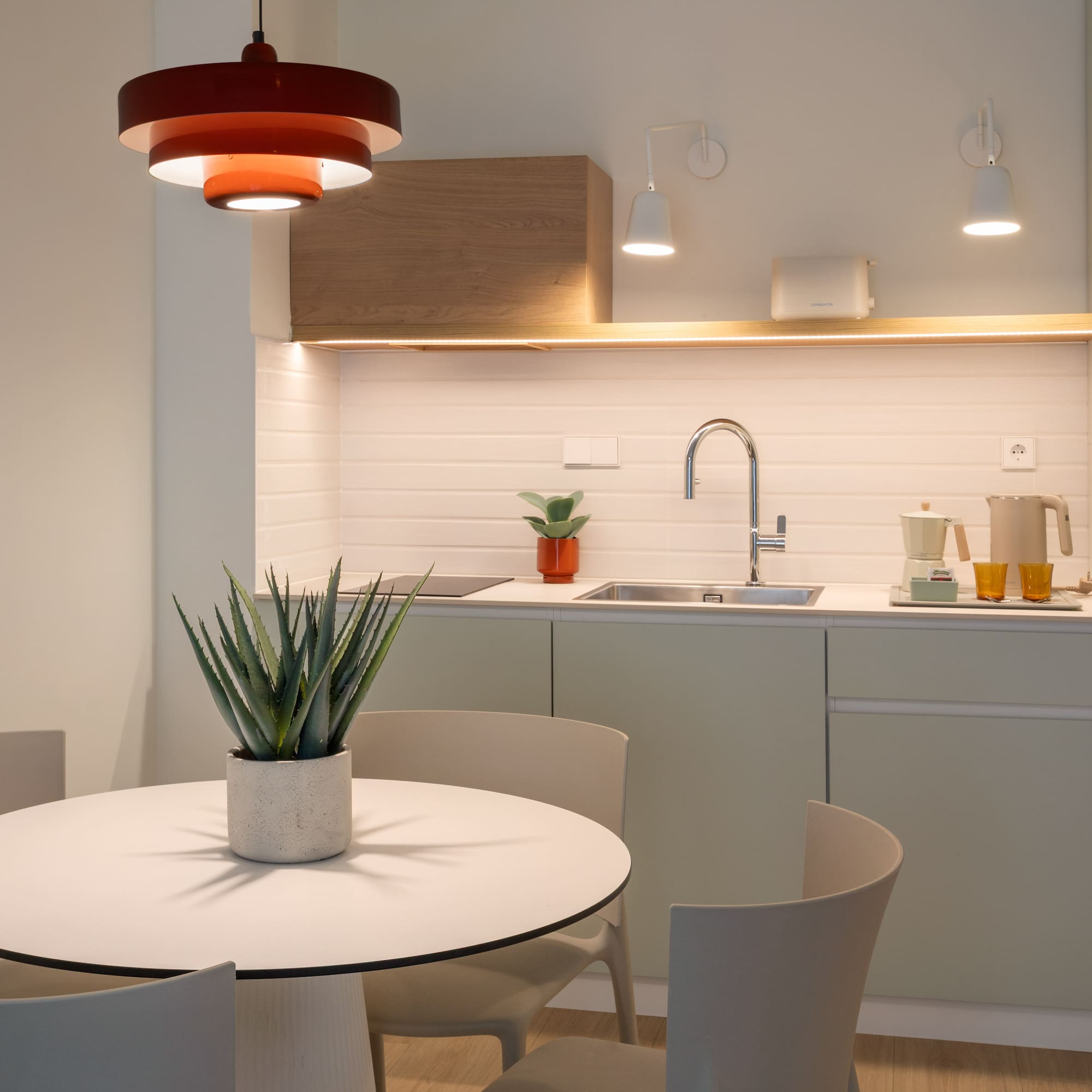 Modern kitchen and dining area with round table and red pendant light.