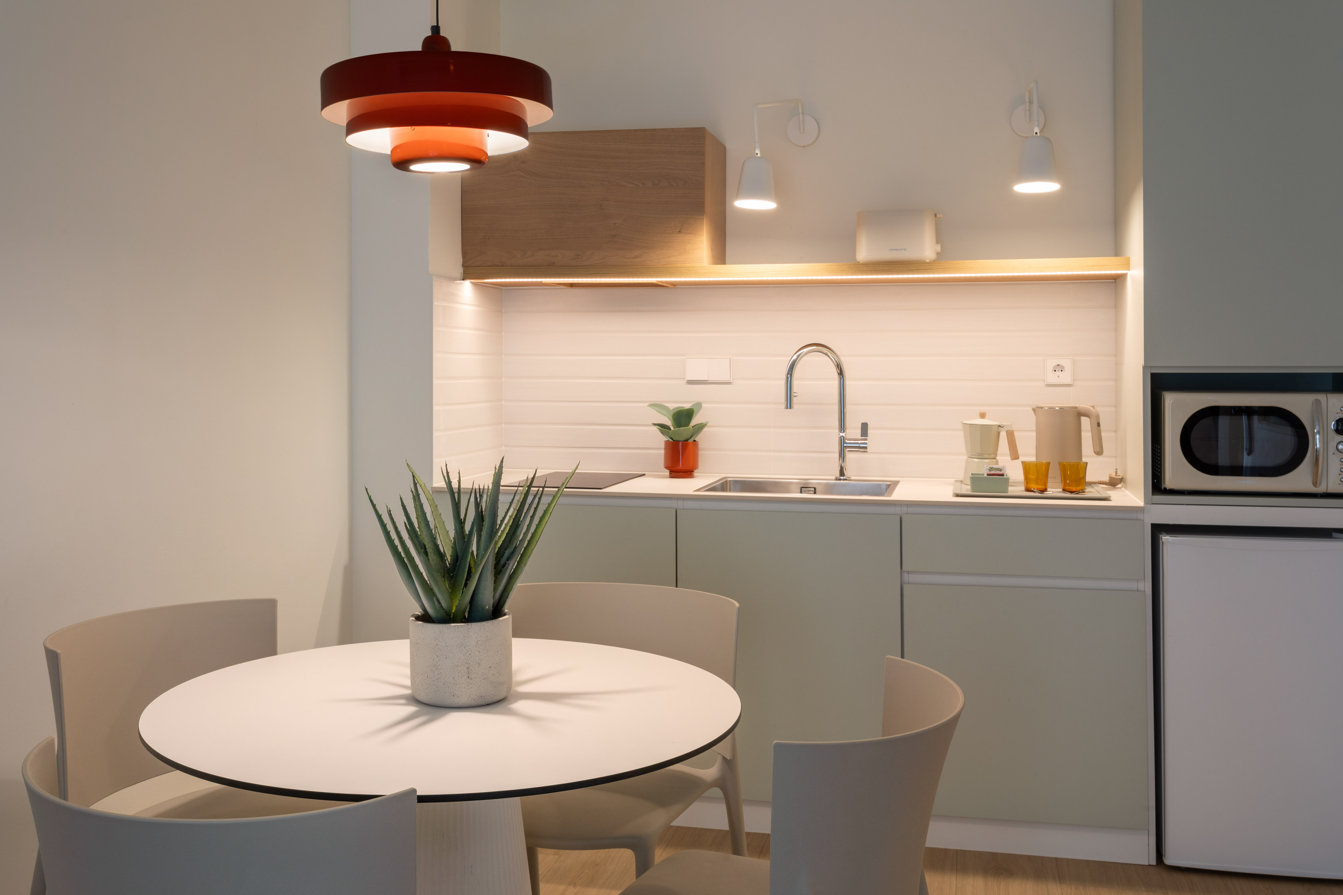 Sleek compact kitchen and dining with red pendant light, white table, appliances.