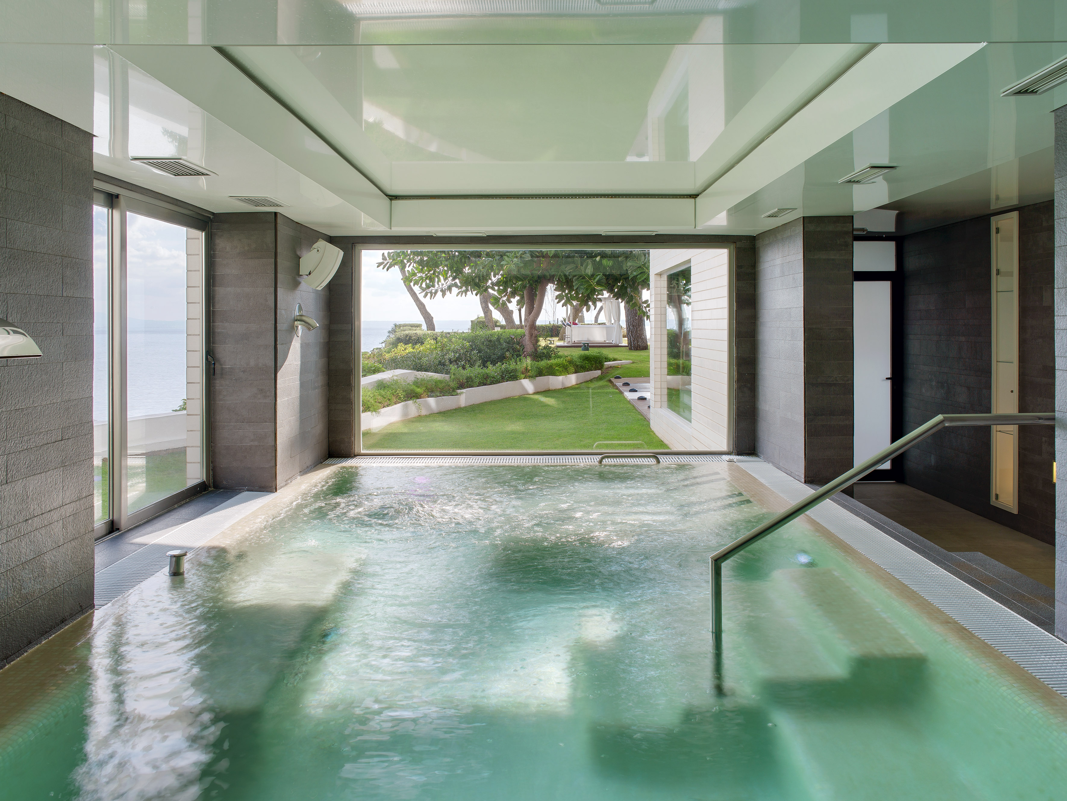 Modern indoor spa pool with bubbling water, coastal garden, and ocean view.