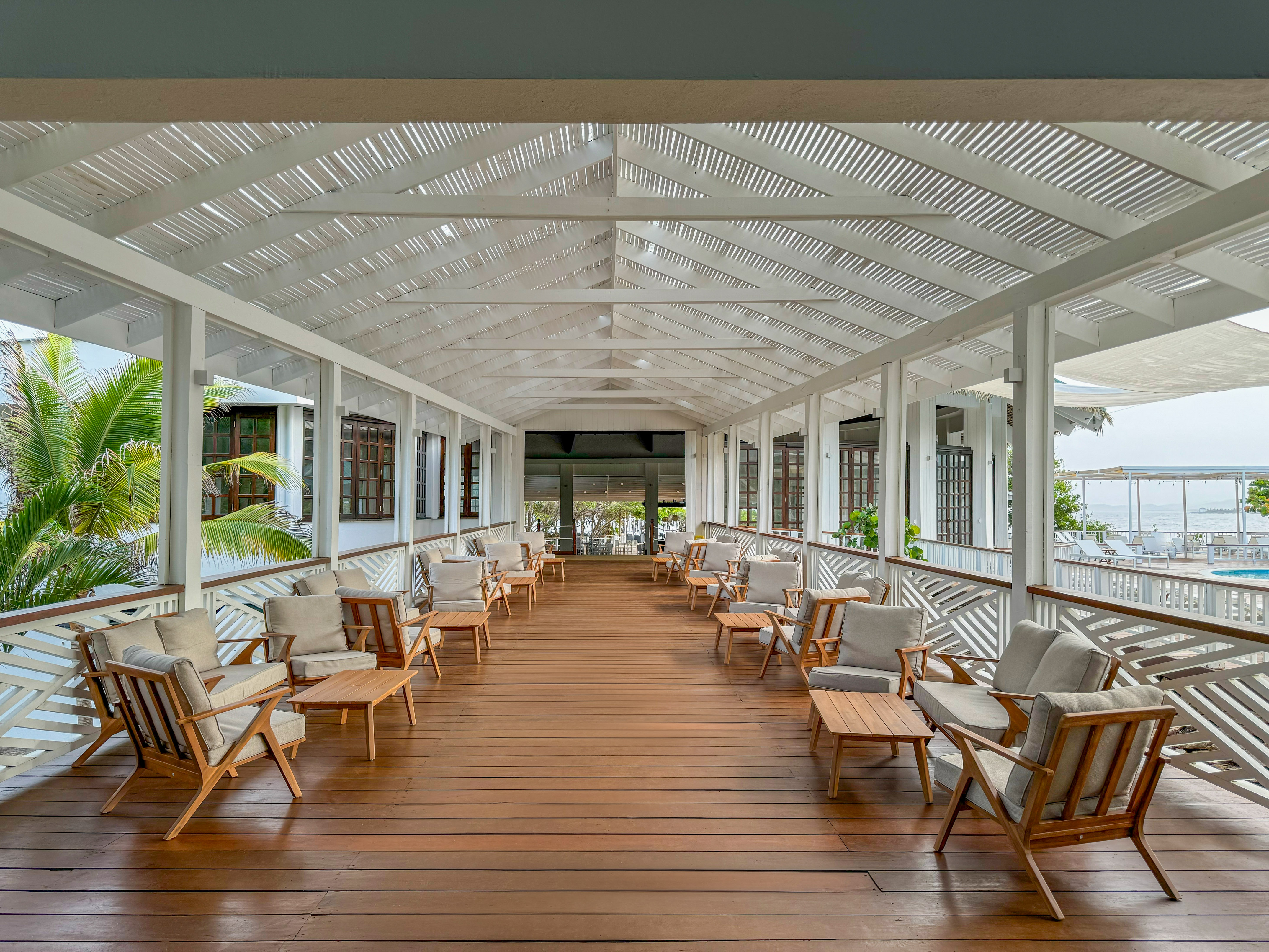 Open-air resort lounge with wooden seating, white slatted roof, and ocean view.