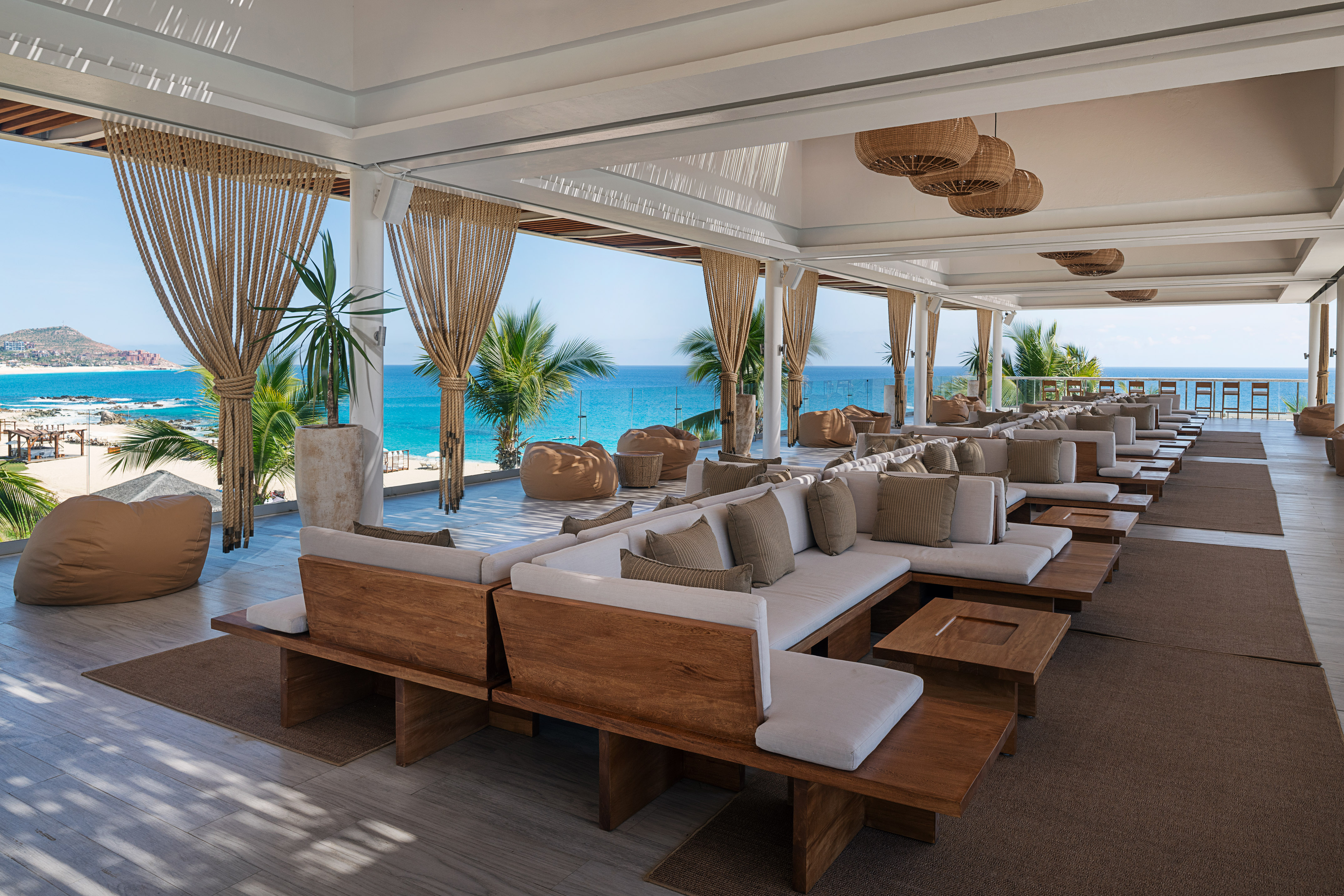 Outdoor lounge with ocean view, modern wooden sofas, and palm trees.