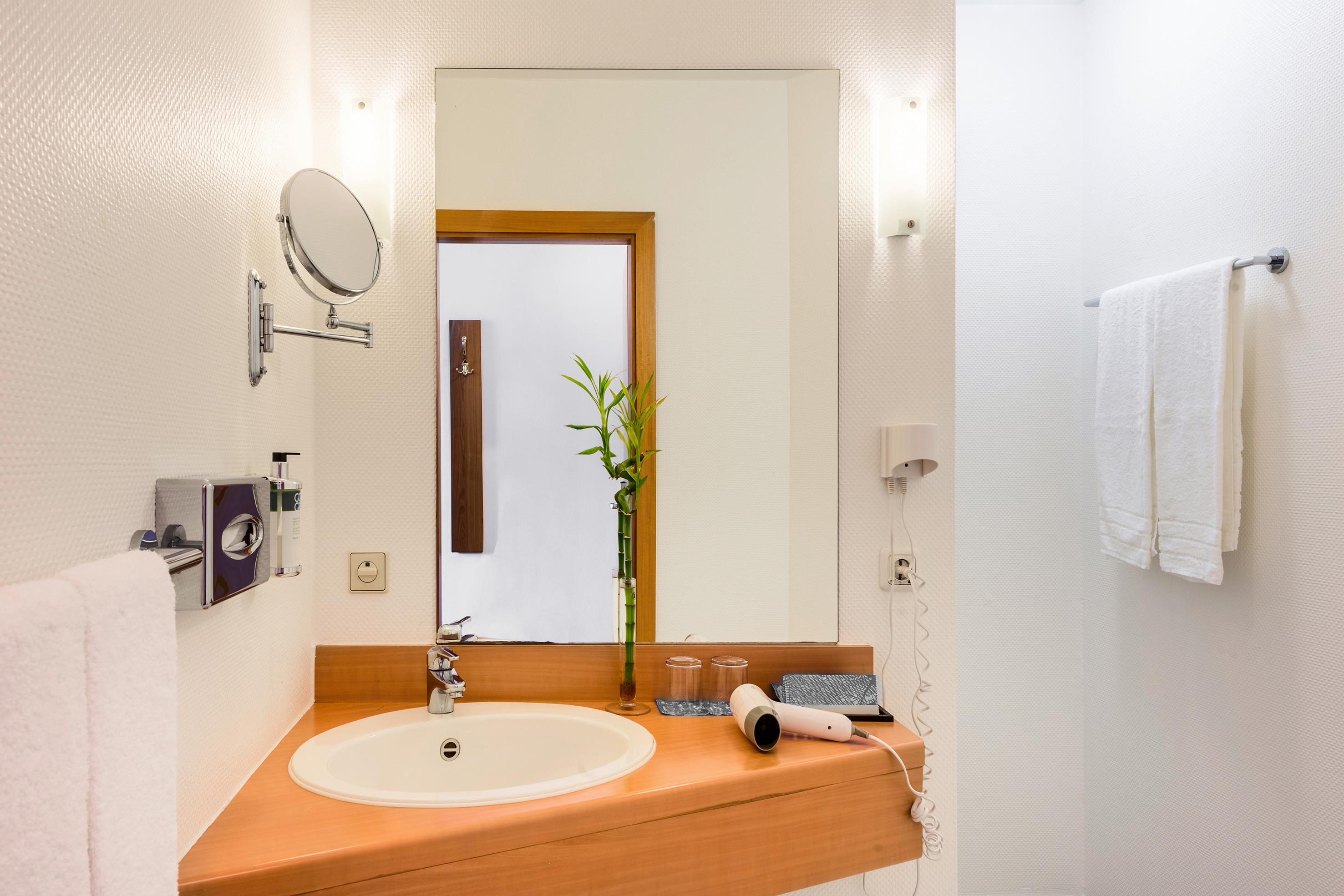 Modern hotel bathroom with wood vanity, sink, mirror, white towels, and hairdryer.