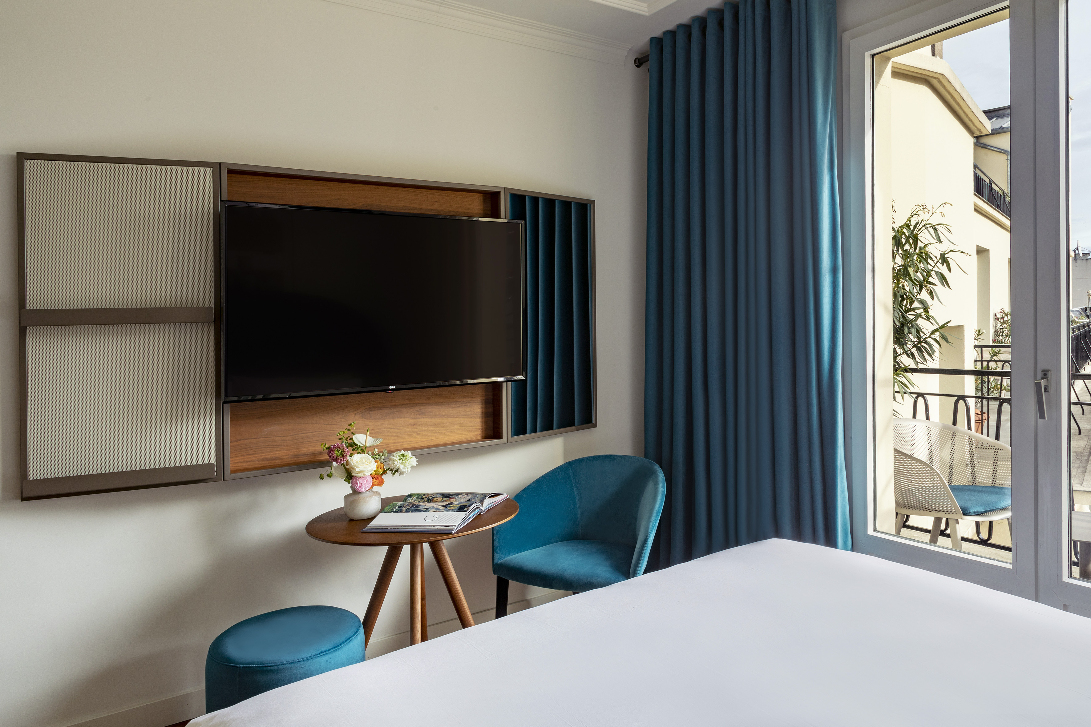 Modern bedroom with mounted TV, teal chair, small table, and balcony view.