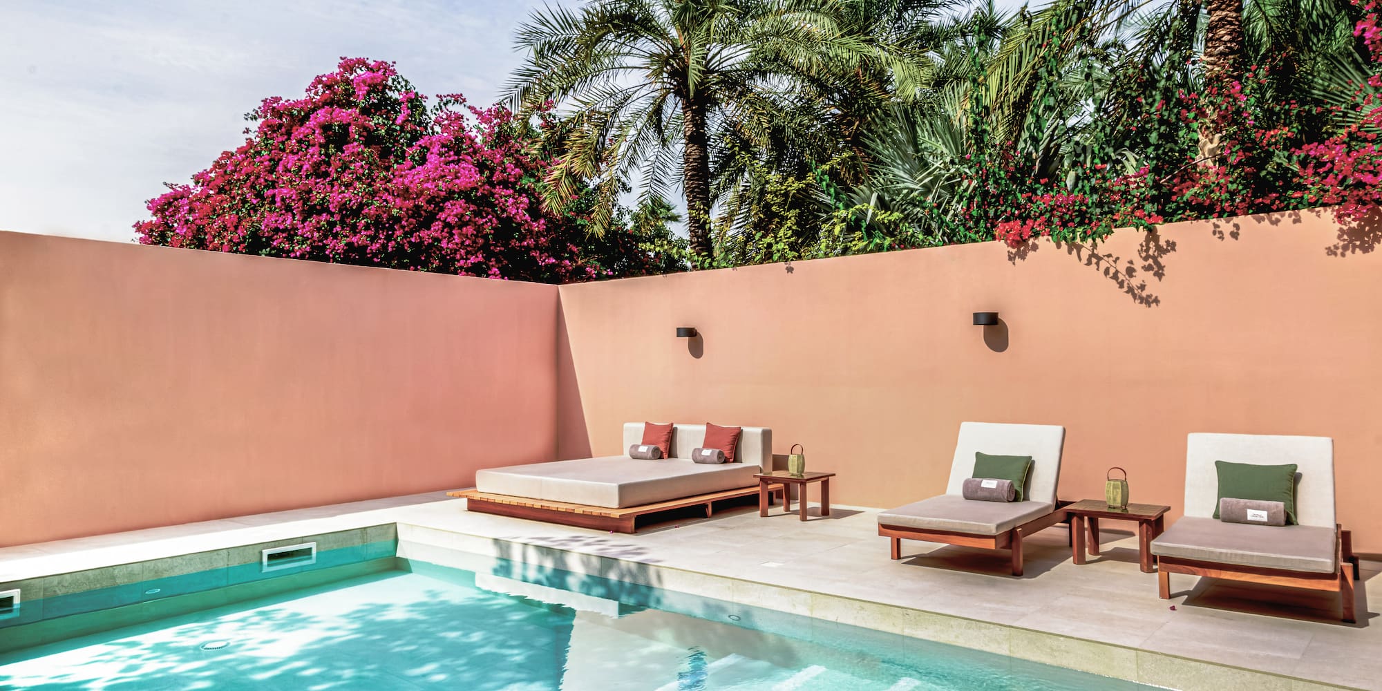 a pool with lounge chairs and a pink wall