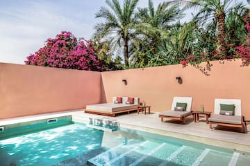 a pool with lounge chairs and a pink wall