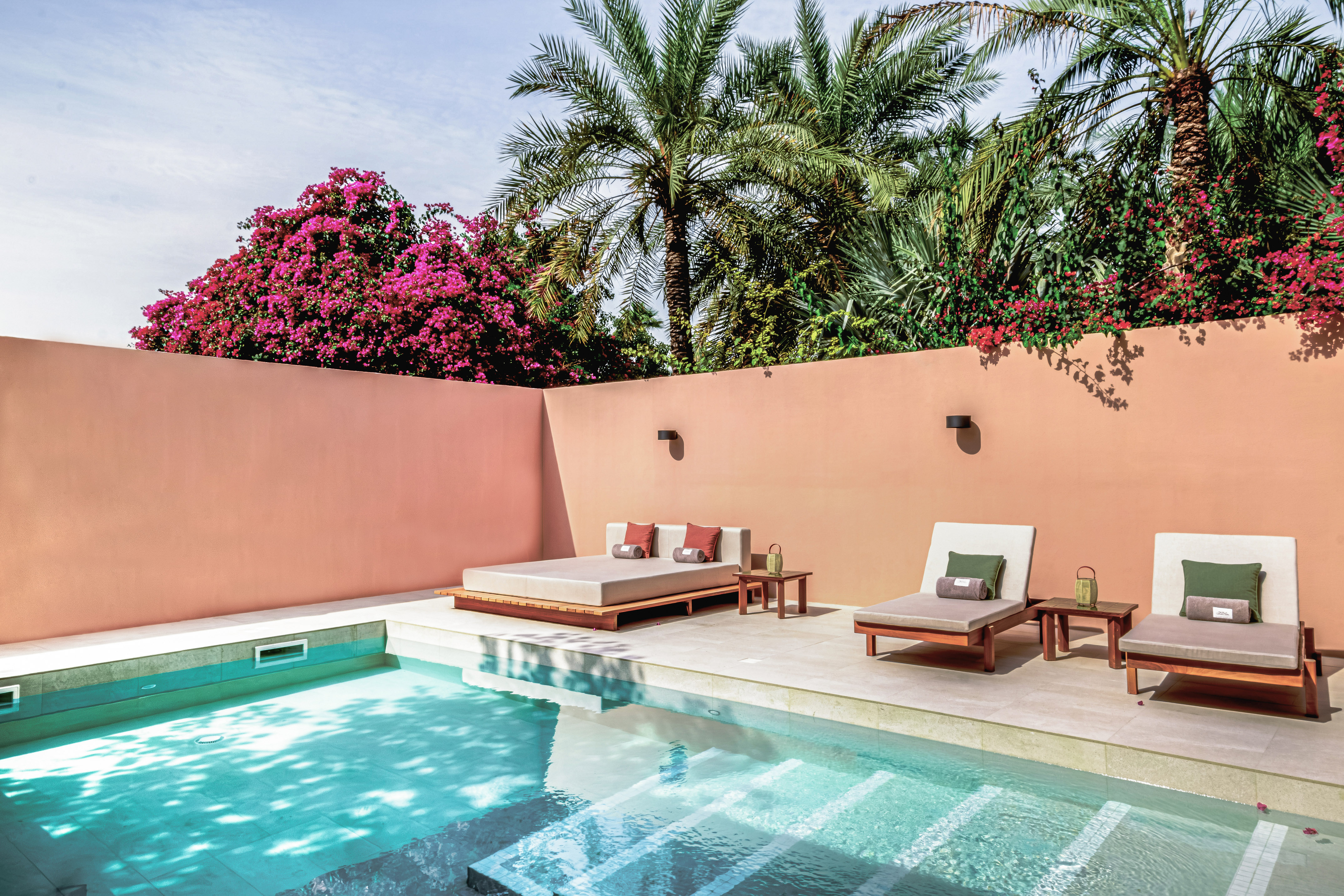 a pool with lounge chairs and a pink wall