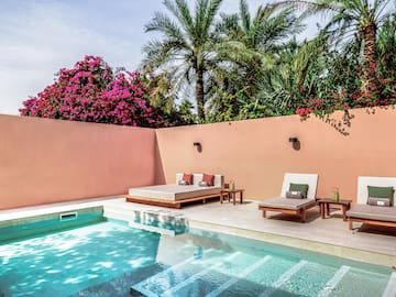 a pool with lounge chairs and a pink wall