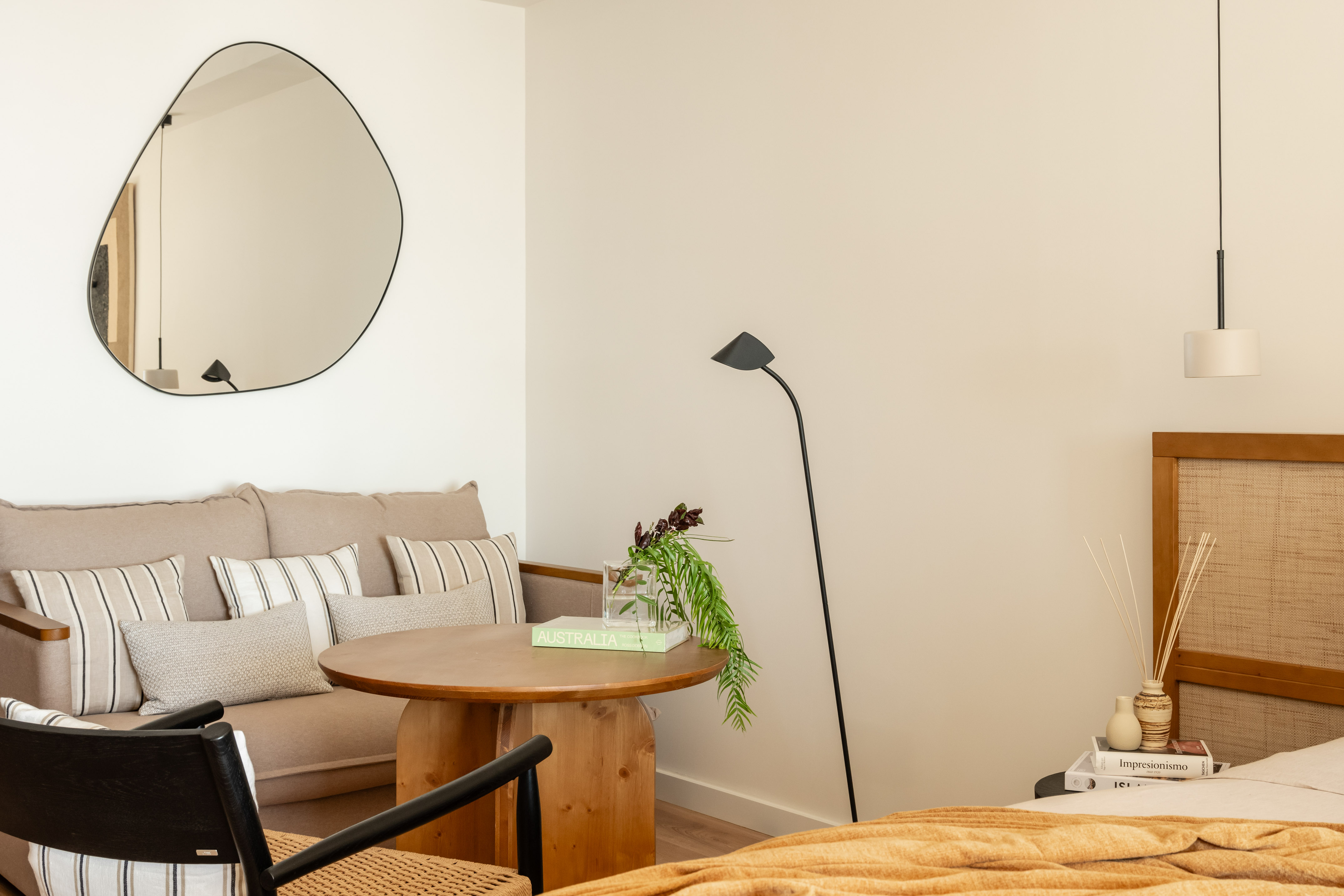 Cozy modern studio with beige sofa, wood table, organic mirror, rattan headboard.