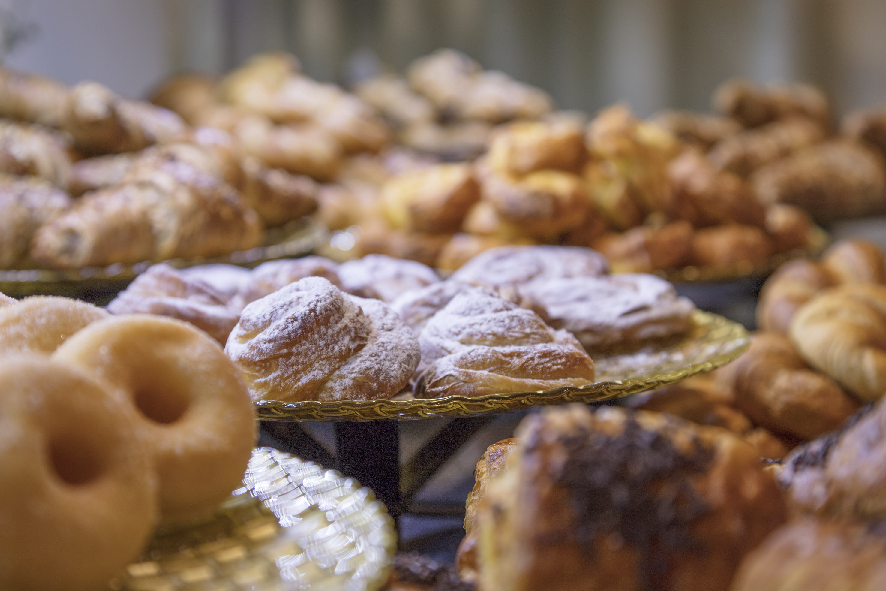 Bakery display of assorted pastries: sugar-dusted swirls, croissants, and donuts.