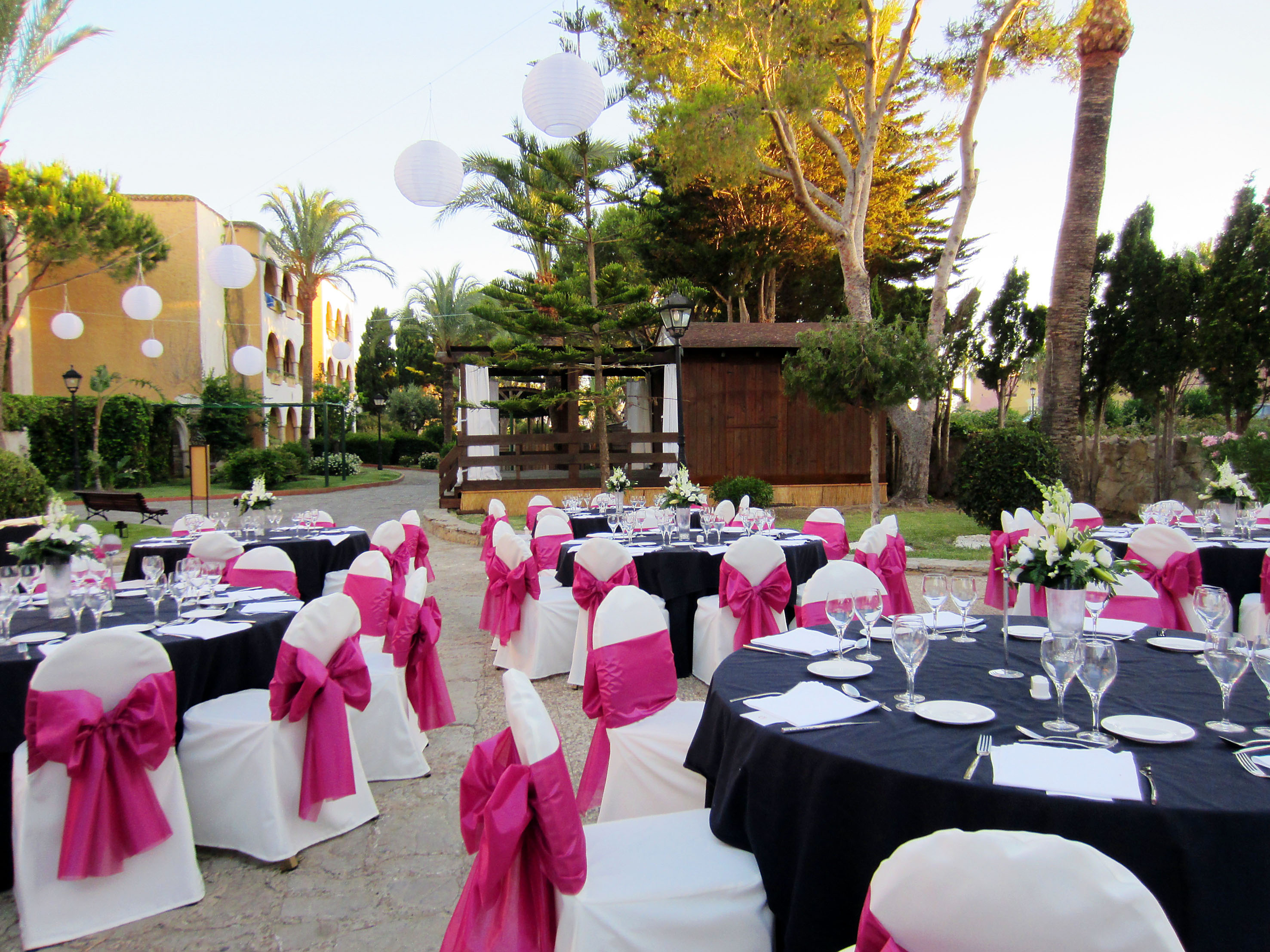 Resort garden reception: black tables, fuchsia chairs, white lanterns, palm trees.