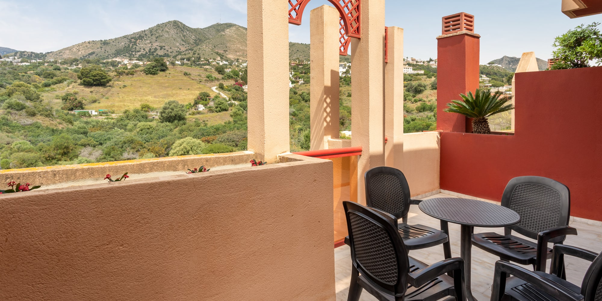 Mediterranean terrace with mountain view, outdoor seating, and red architectural details.