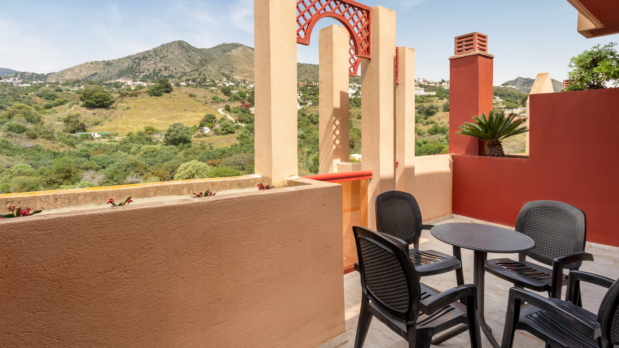 Mediterranean balcony with outdoor seating, mountain view, and red arch details.