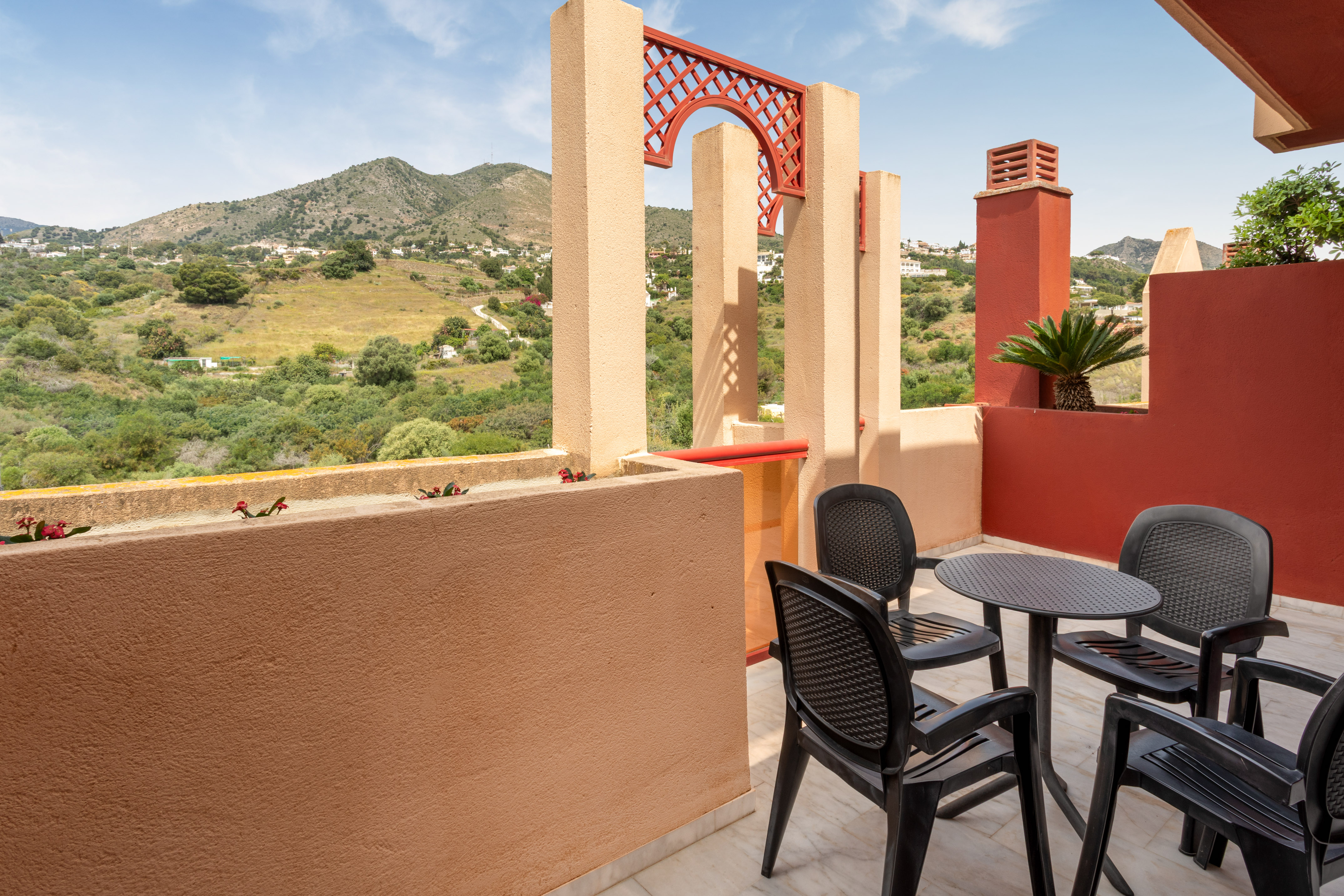 Mediterranean balcony with outdoor seating, mountain view, and red arch details.