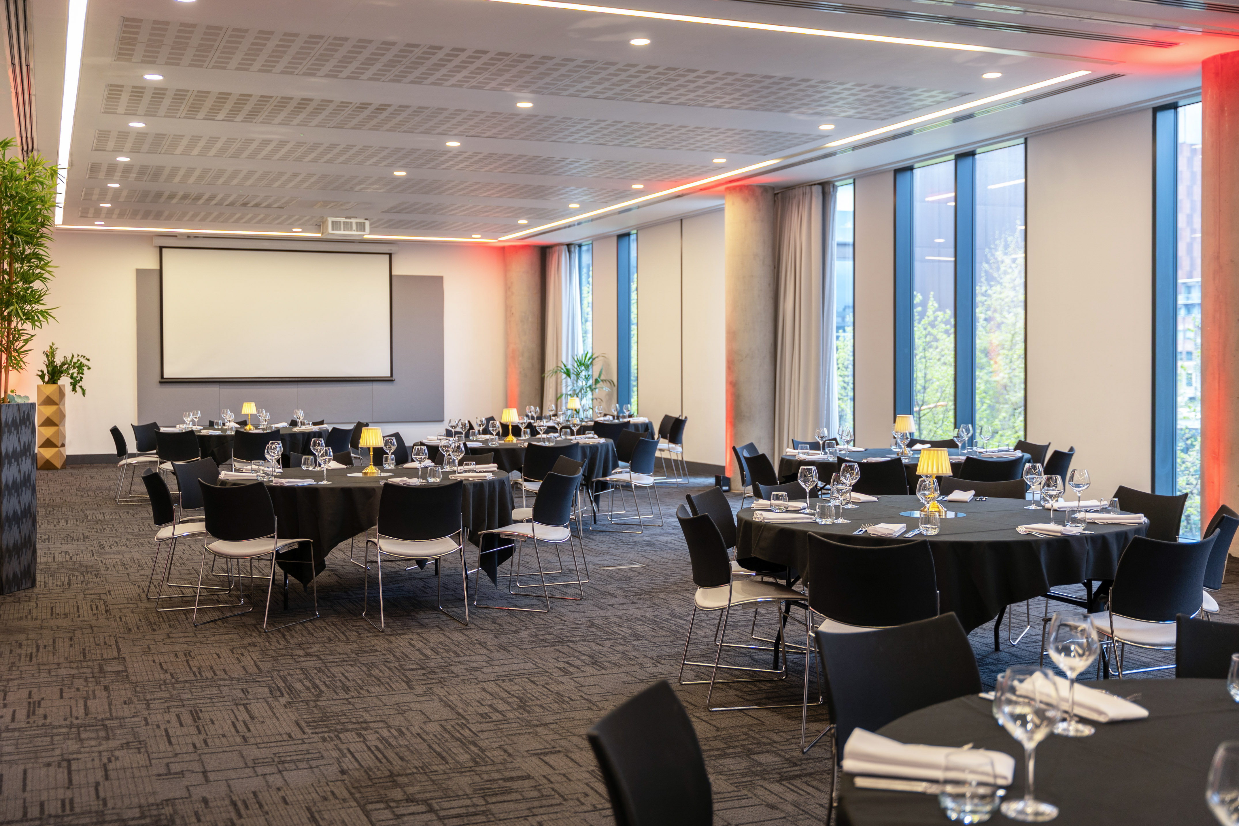 Modern event space with set round tables, screen, and red accent lighting.
