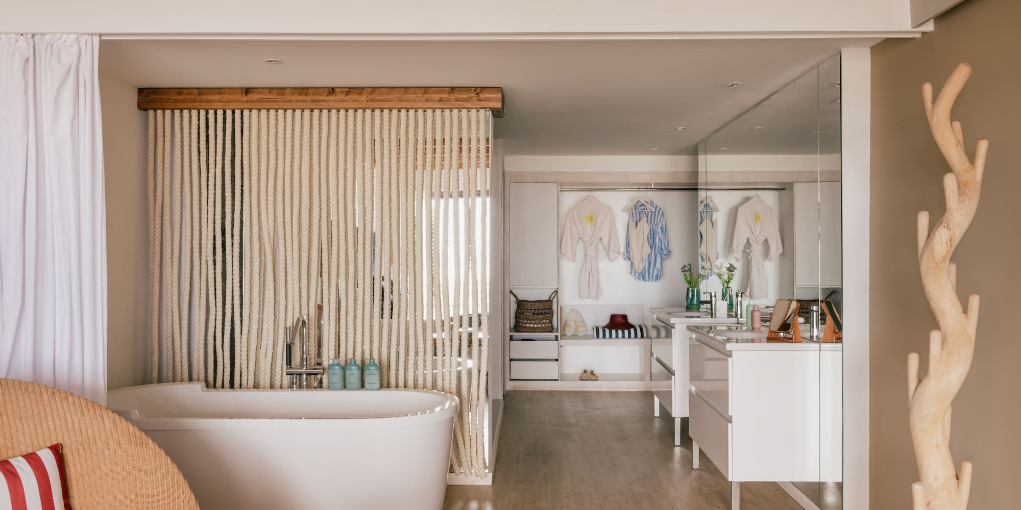 Spa-like open bathroom with white tub, rope screen, wooden beams, and vanity.