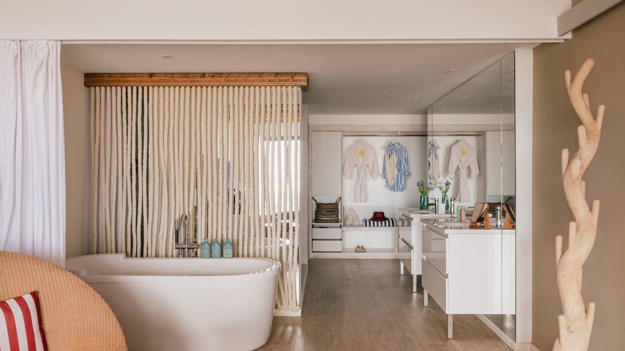 Spa-like open bathroom with white tub, rope screen, wooden beams, and vanity.