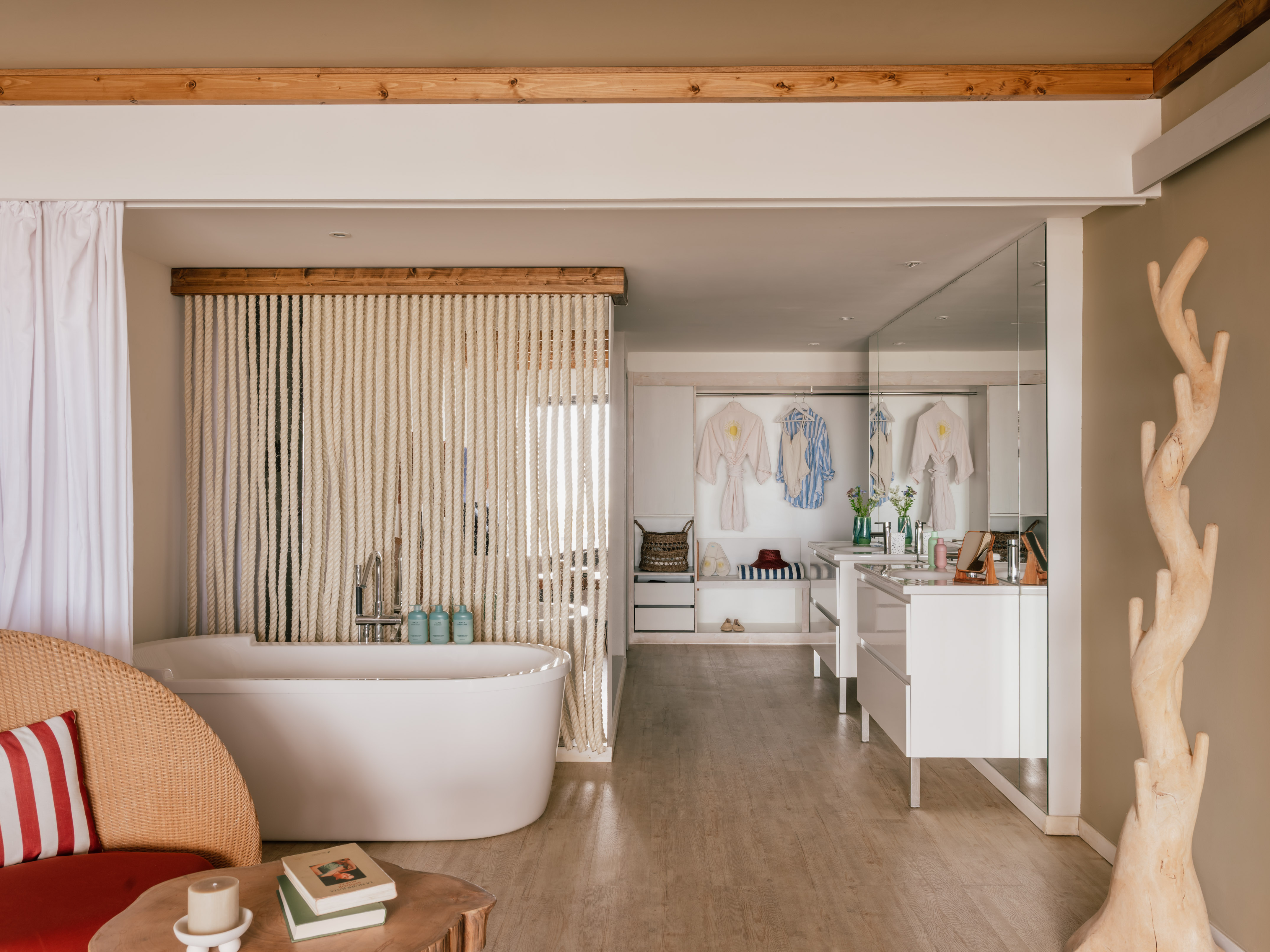 Spa-like open bathroom with white tub, rope screen, wooden beams, and vanity.