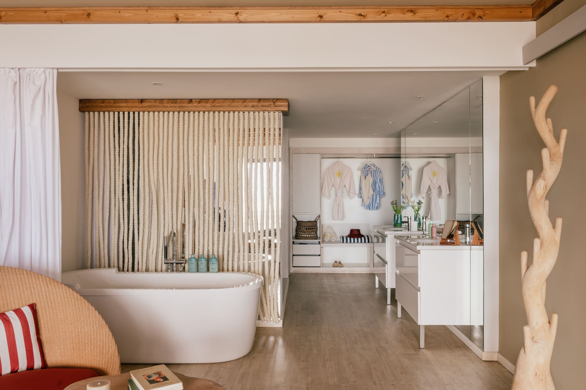 Spa-like open bathroom with white tub, rope screen, wooden beams, and vanity.