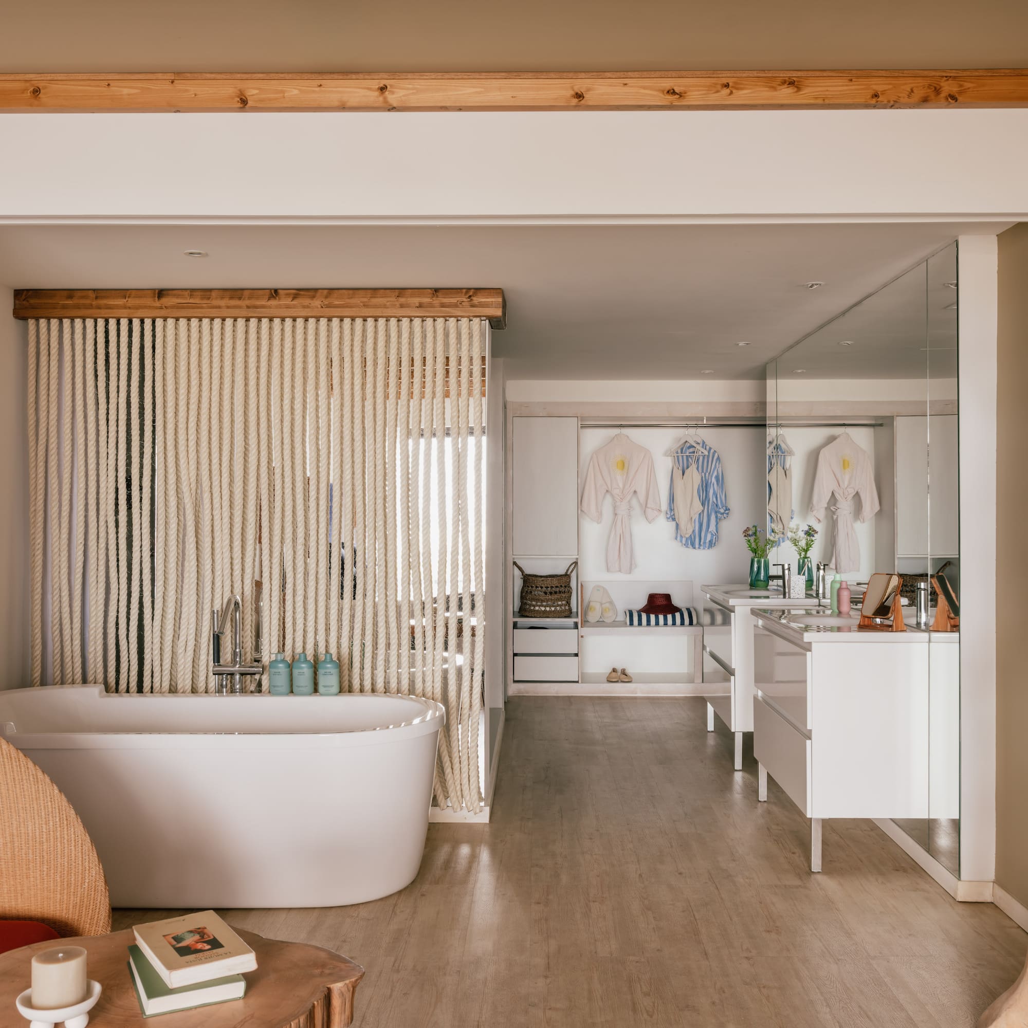 Spa-like open bathroom with white tub, rope screen, wooden beams, and vanity.