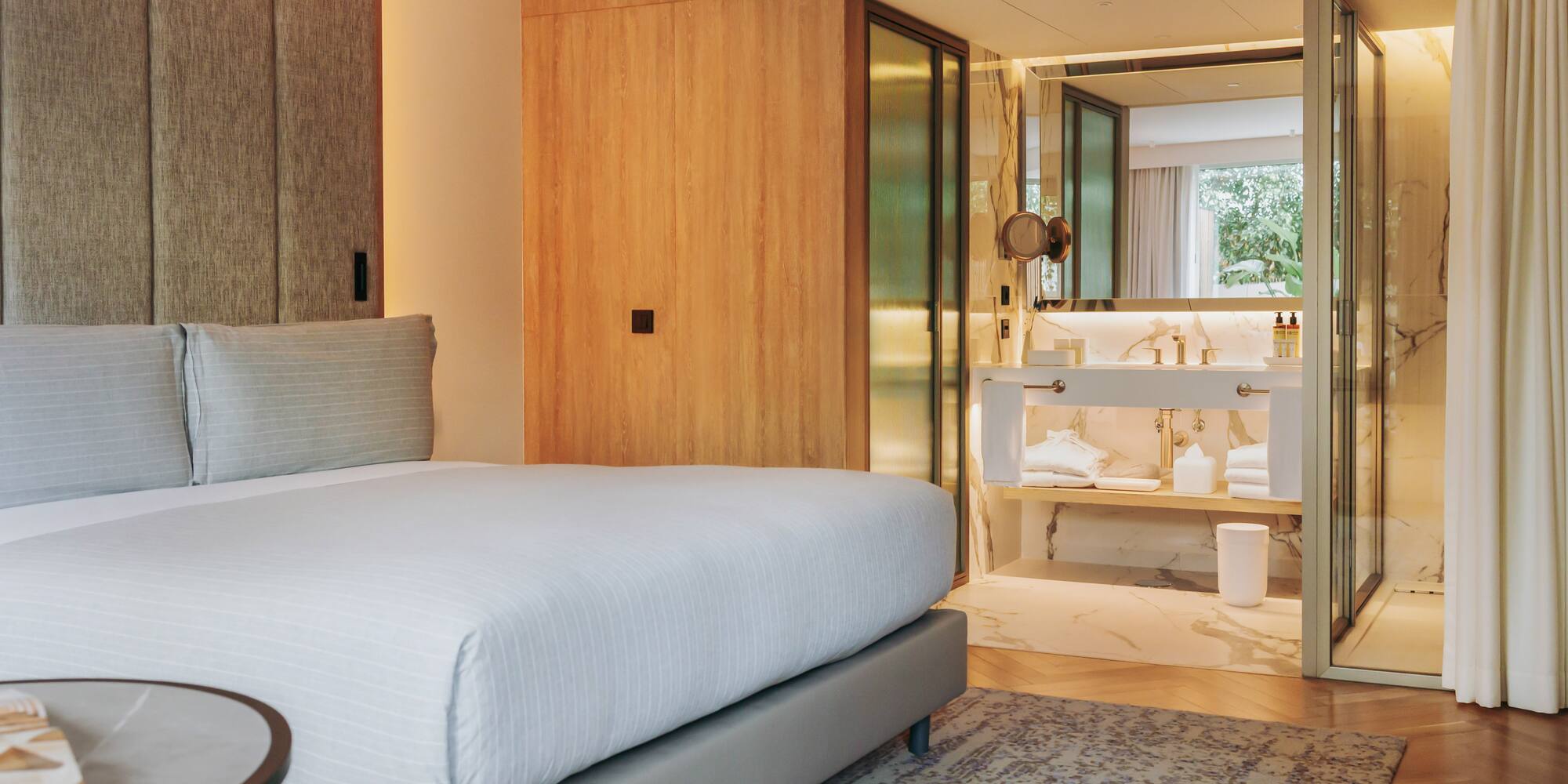 Modern hotel bedroom with king bed and open marble ensuite bathroom.