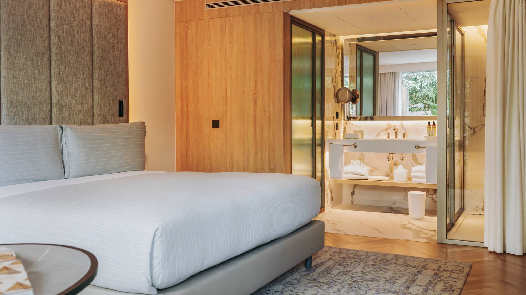 Modern hotel bedroom with king bed and open marble ensuite bathroom.